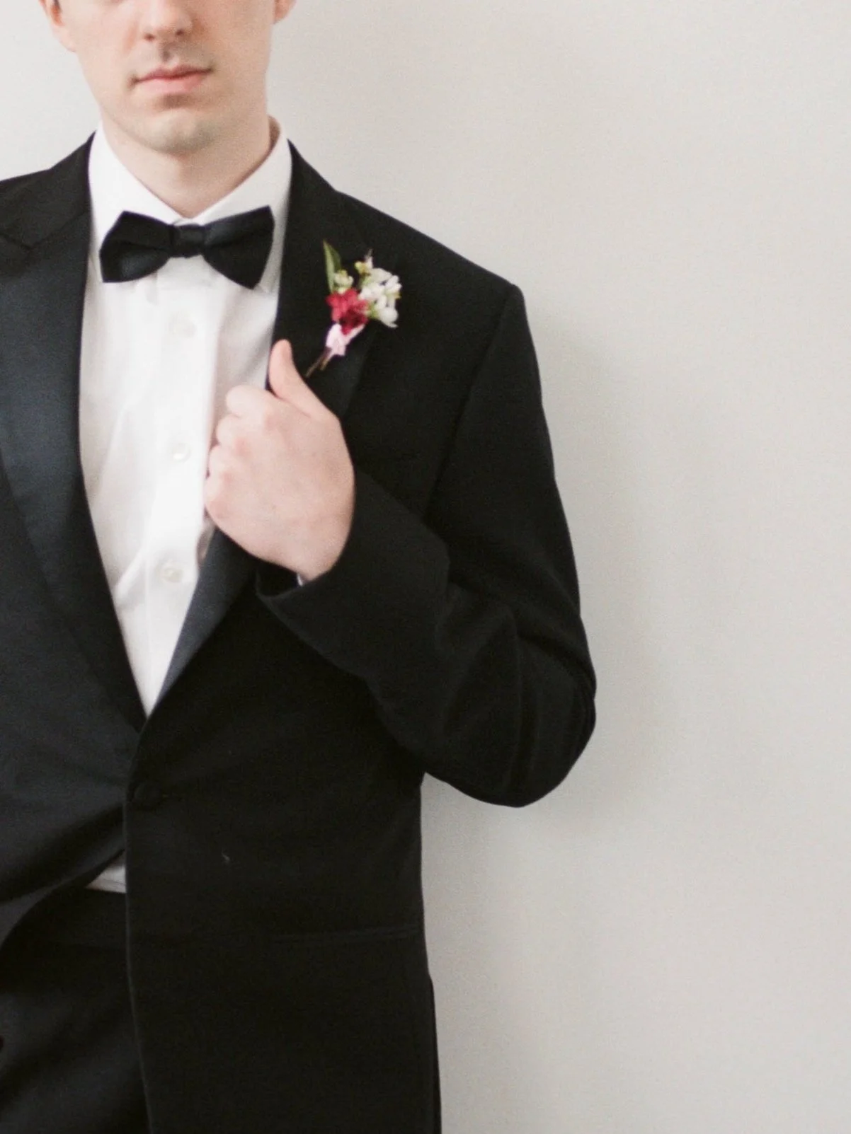 Groom in a black tuxedo with a petite red and white floral boutonniere.