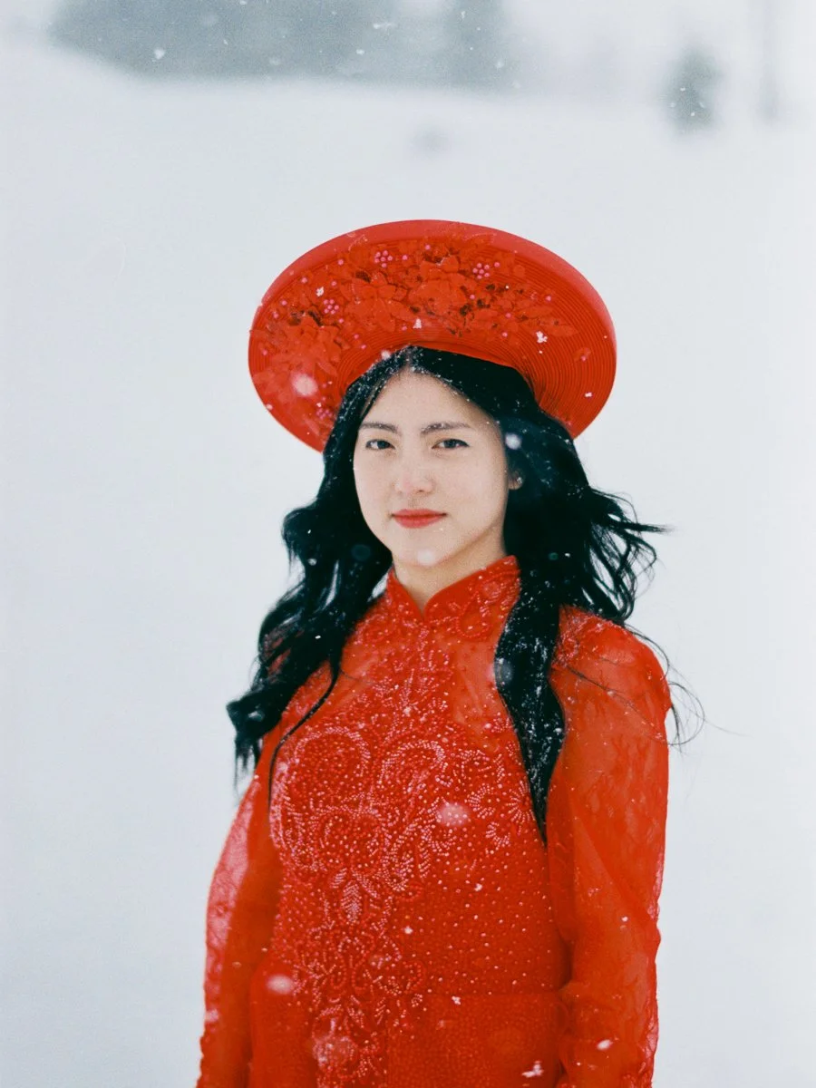 Bride in red Vietnamese áo dài and khăn đóng standing in falling snow at Mount Hood.
