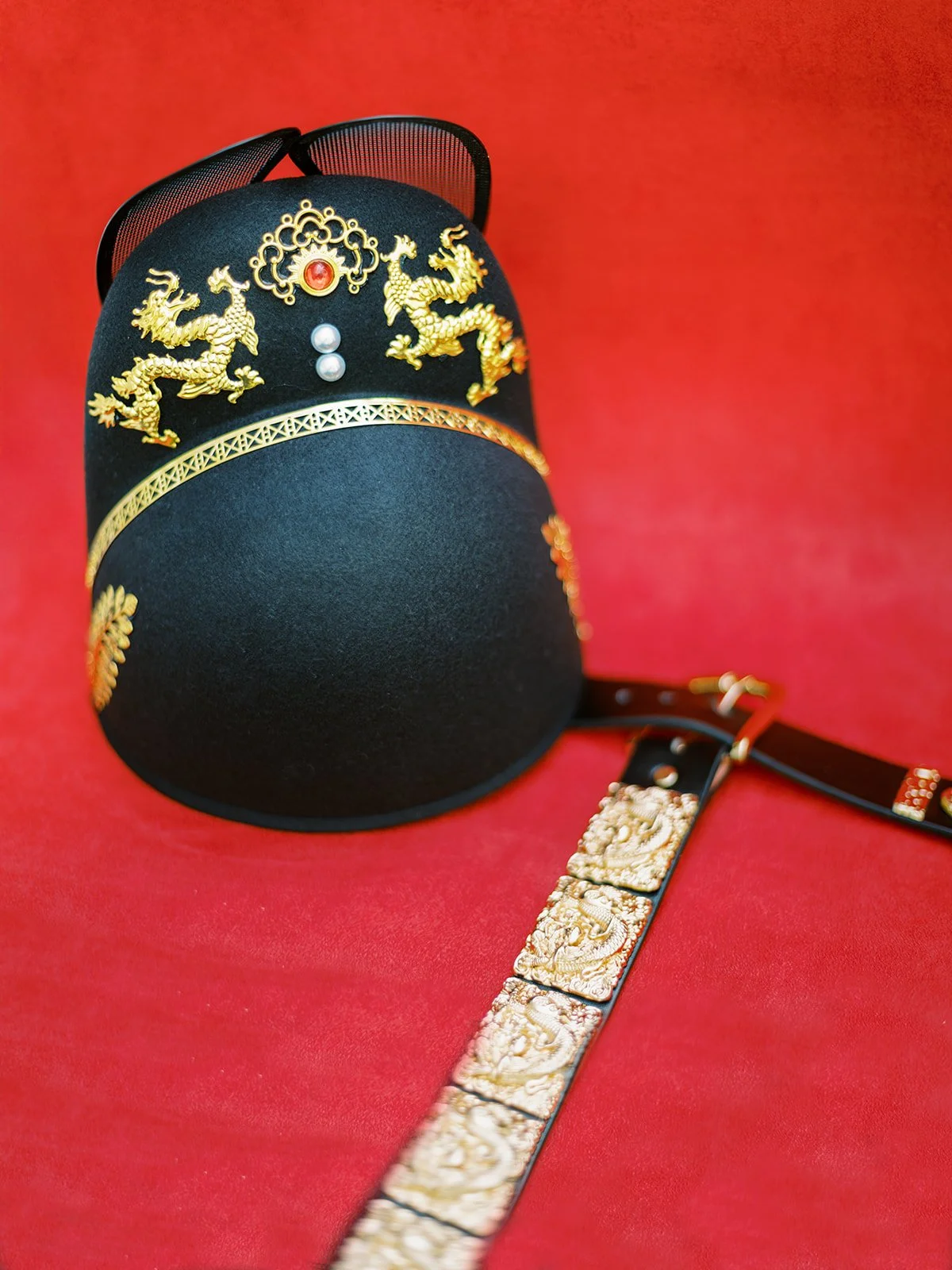 Black ceremonial hat with gold dragon details and decorative belt placed on a red backdrop