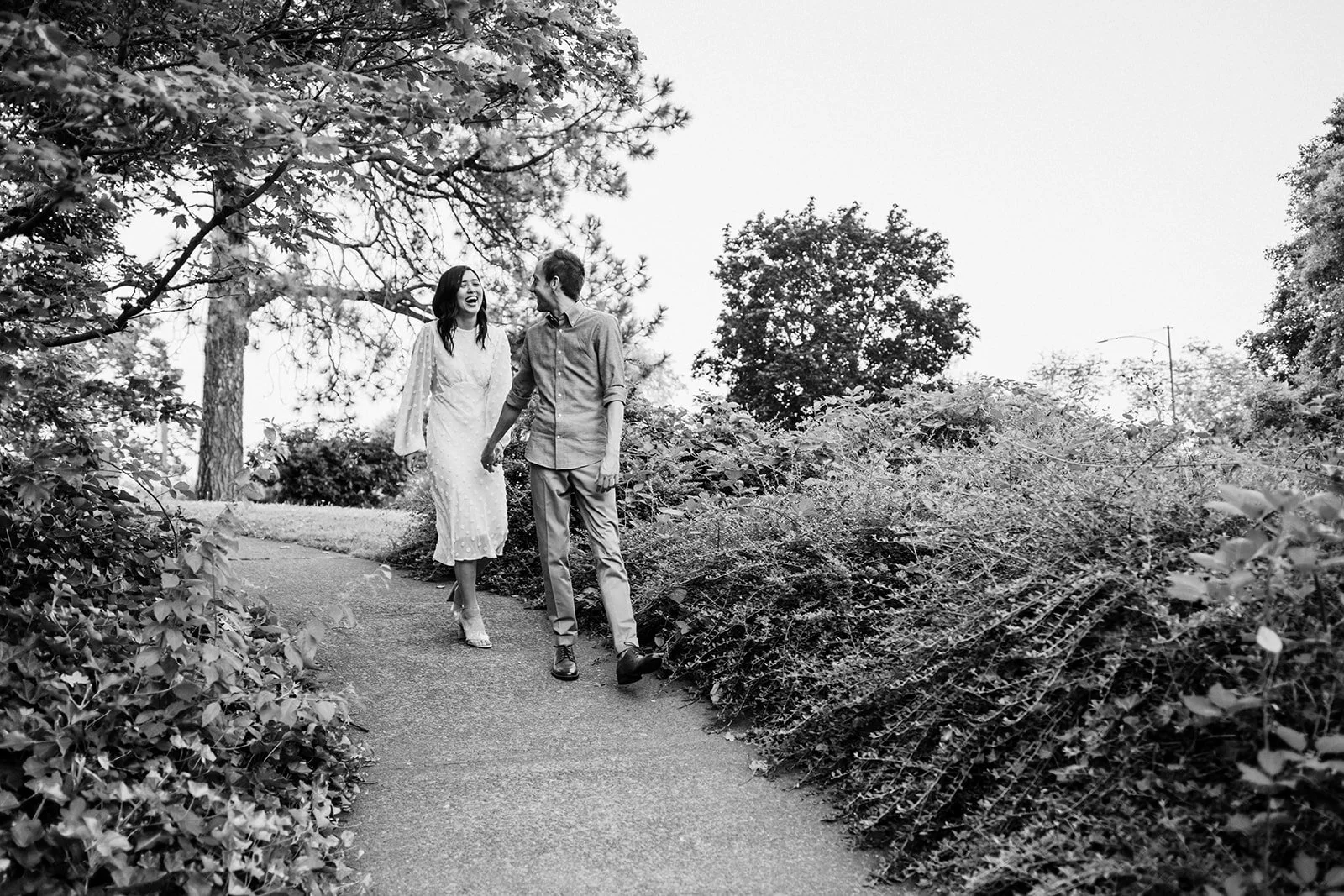 Black and white photo of couple walking hand in hand along a garden path surrounded by lush greenery