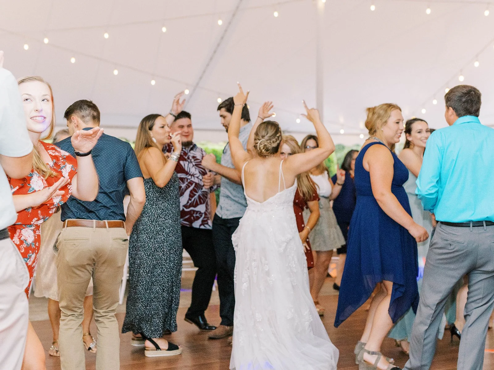 Bride dances with guests under string lights at the wedding reception tent.