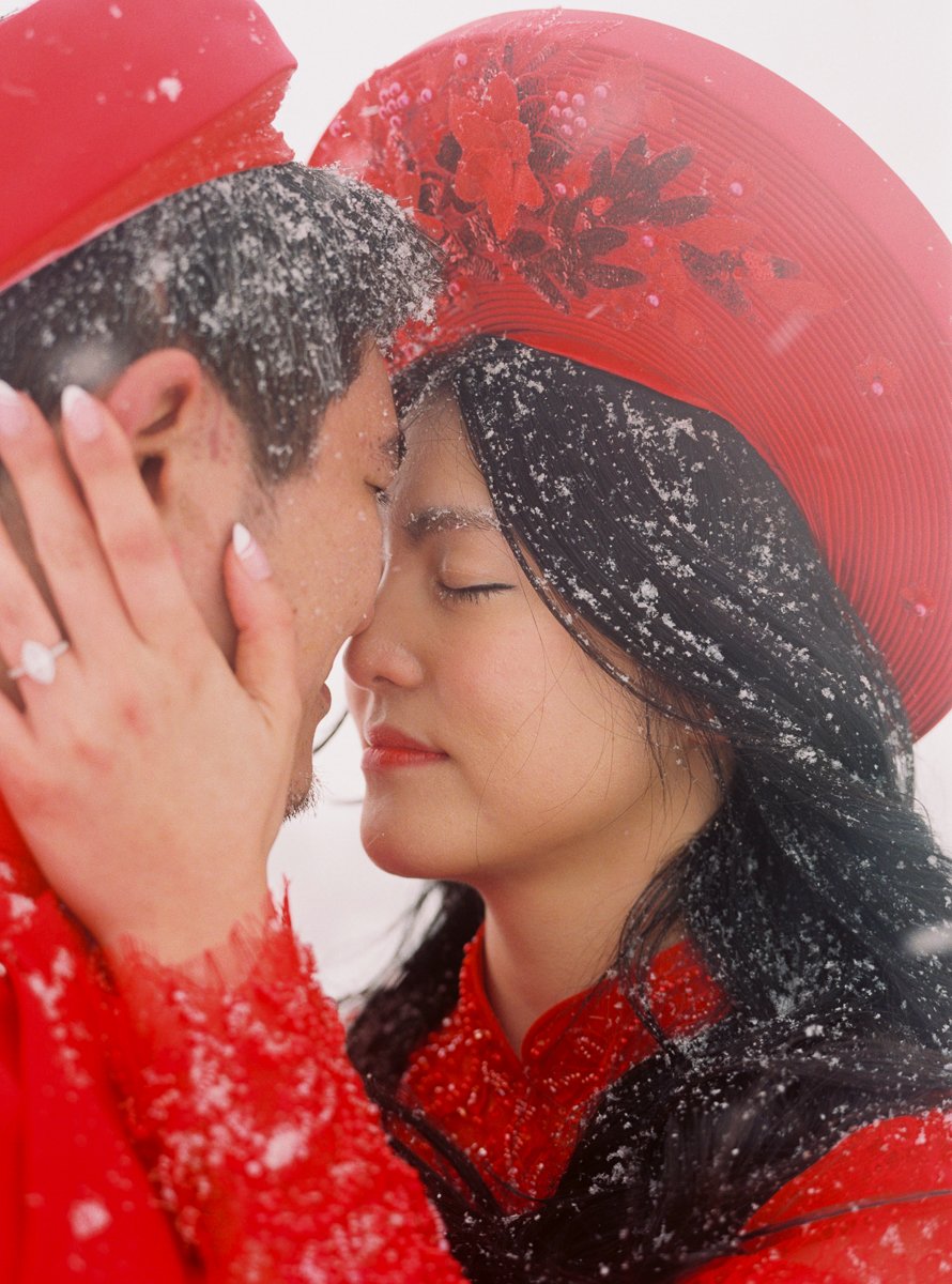 Couple wearing red Vietnamese attire embracing in falling snow during a Mount Hood portrait session.