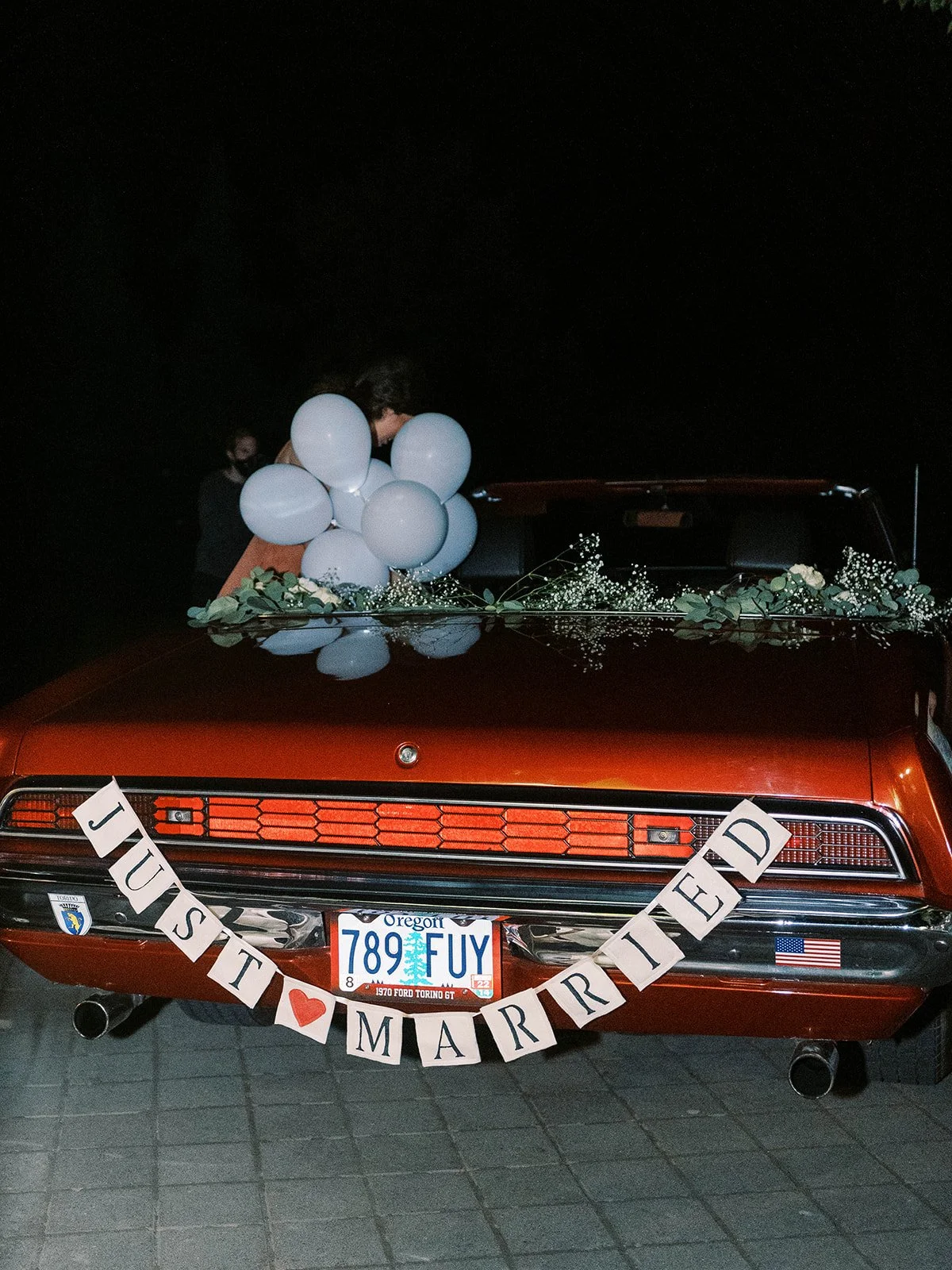 Vintage red convertible decorated with “Just Married” sign and balloons at wedding exit