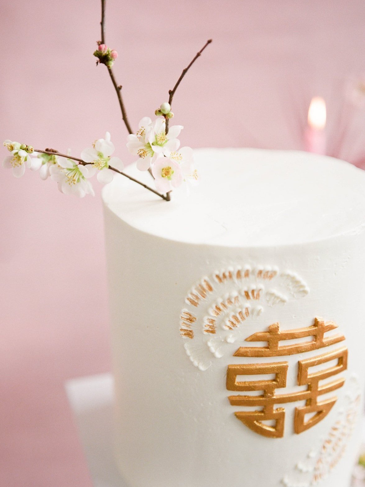 White wedding cake decorated with a gold Chinese double-happiness symbol and flowering branch.