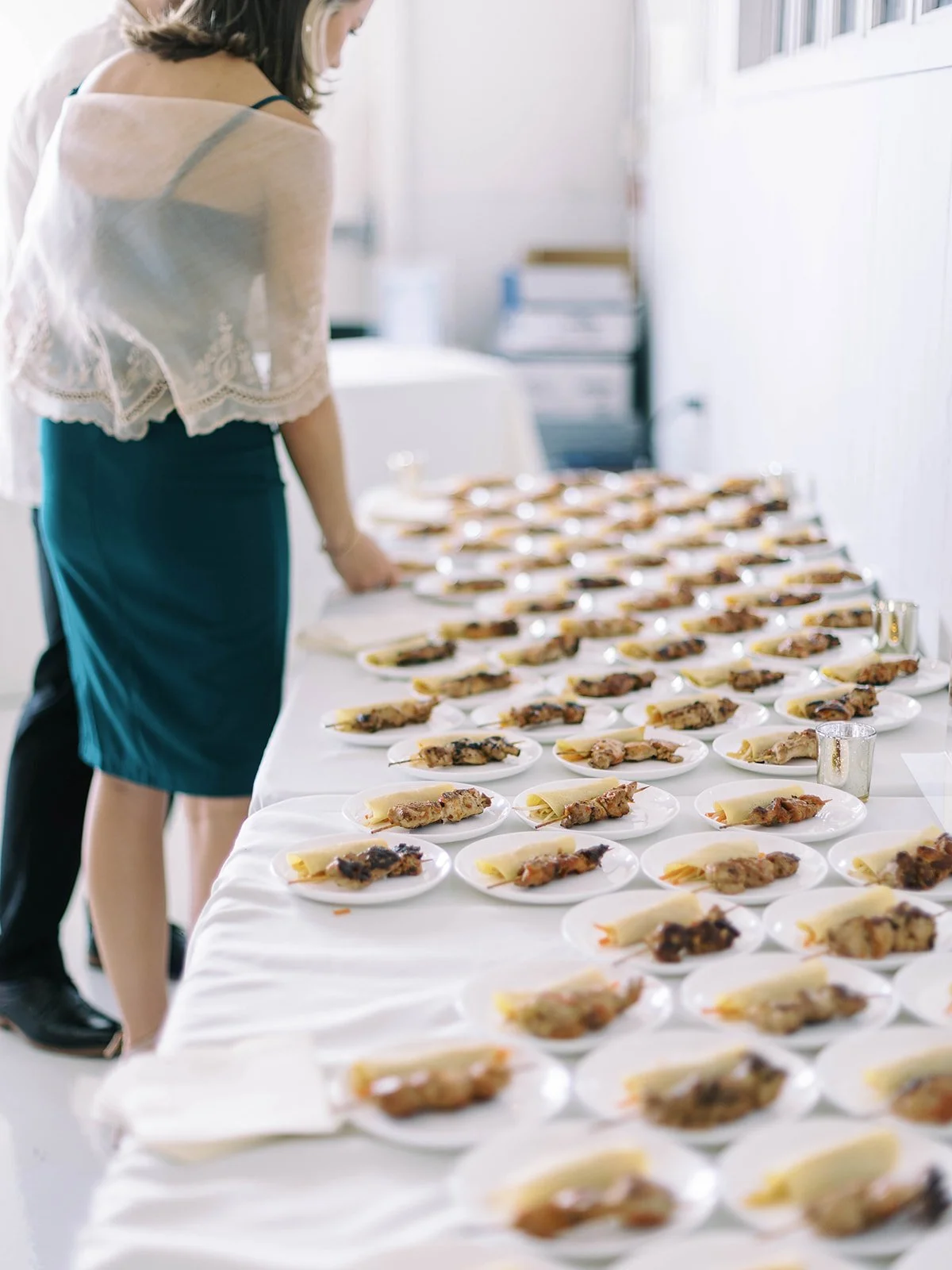Rows of Filipino appetizer plates — chicken skewers and lumpia — on a long table inside the reception venue
