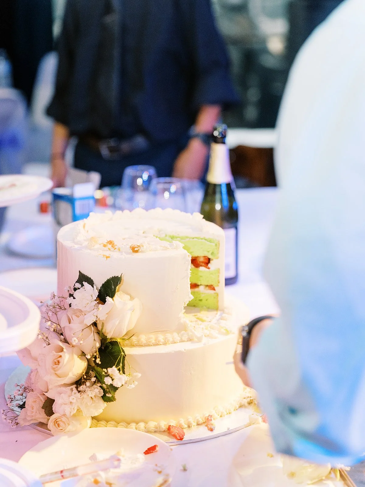Two-tiered white wedding cake decorated with white roses and baby's breath, cut open to reveal green matcha layers with strawberry filling, at the Mekong Bistro reception