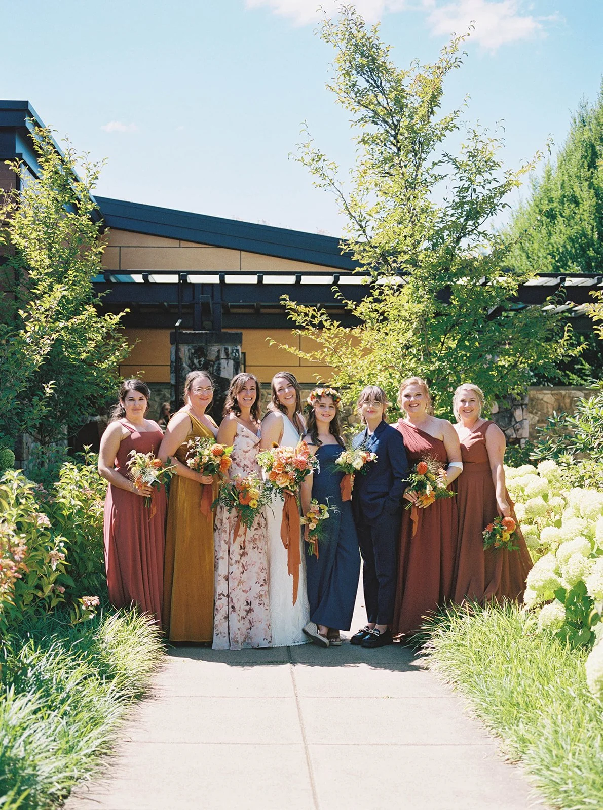 Wedding party standing together outdoors holding bouquets in warm-toned dresses