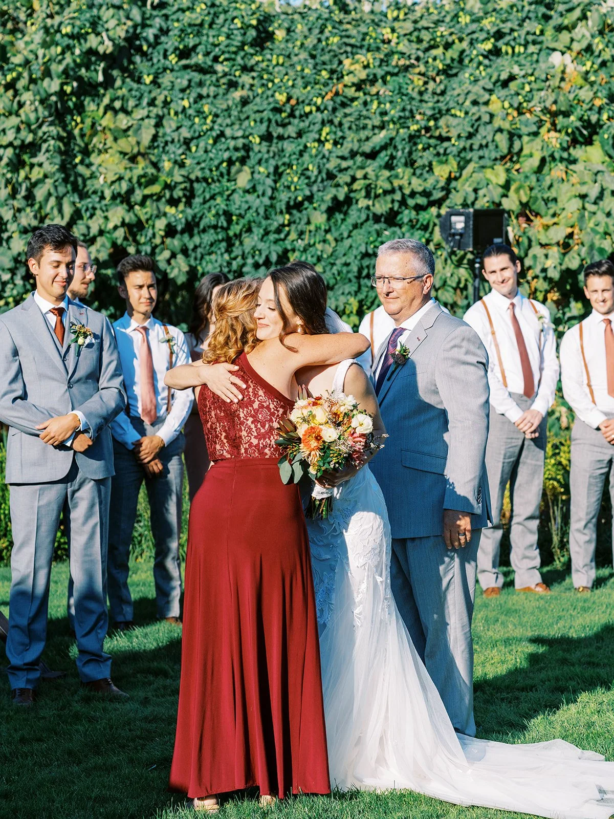 Bride hugging guest during ceremony, groomsmen standing in background