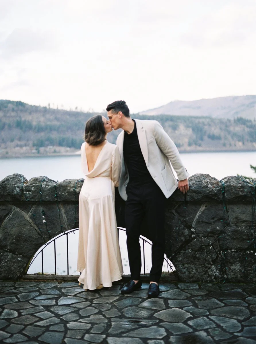 Couple kissing beside stone overlook with river and hills at Columbia Gorge Hotel