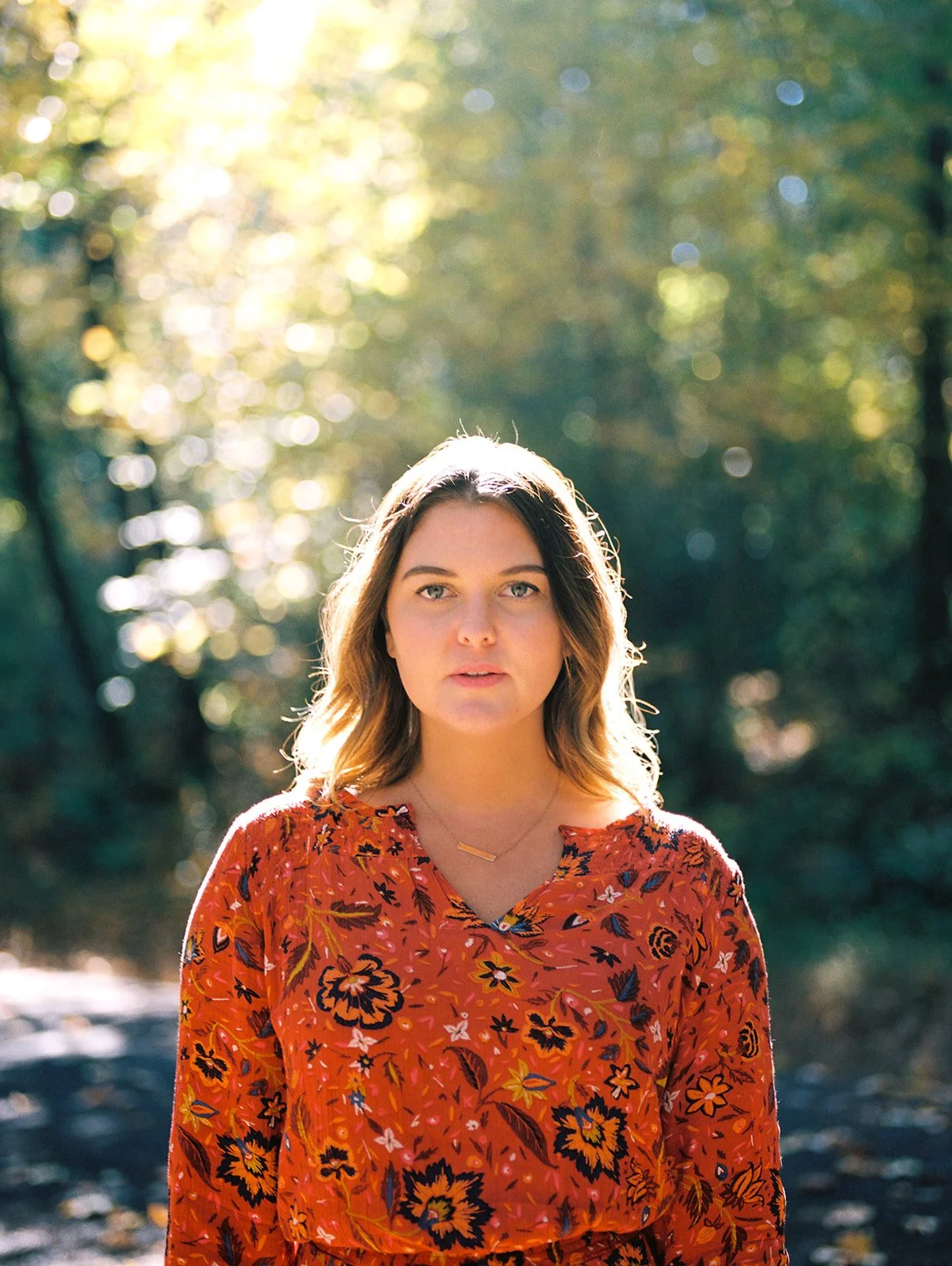 Portrait of woman in red floral dress with soft sunlight and blurred fall forest background in Oregon