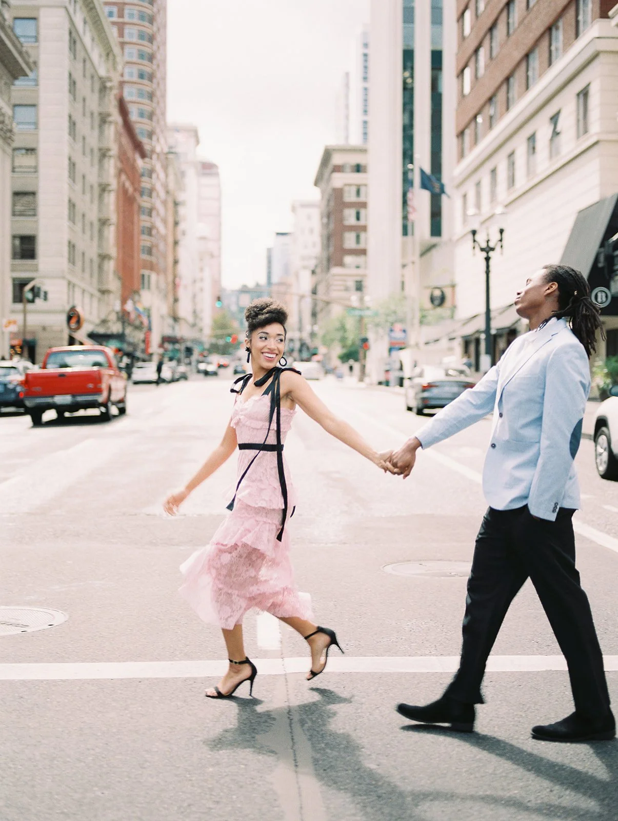 Stylish couple walking hand in hand across a Portland street, buildings and cars in background