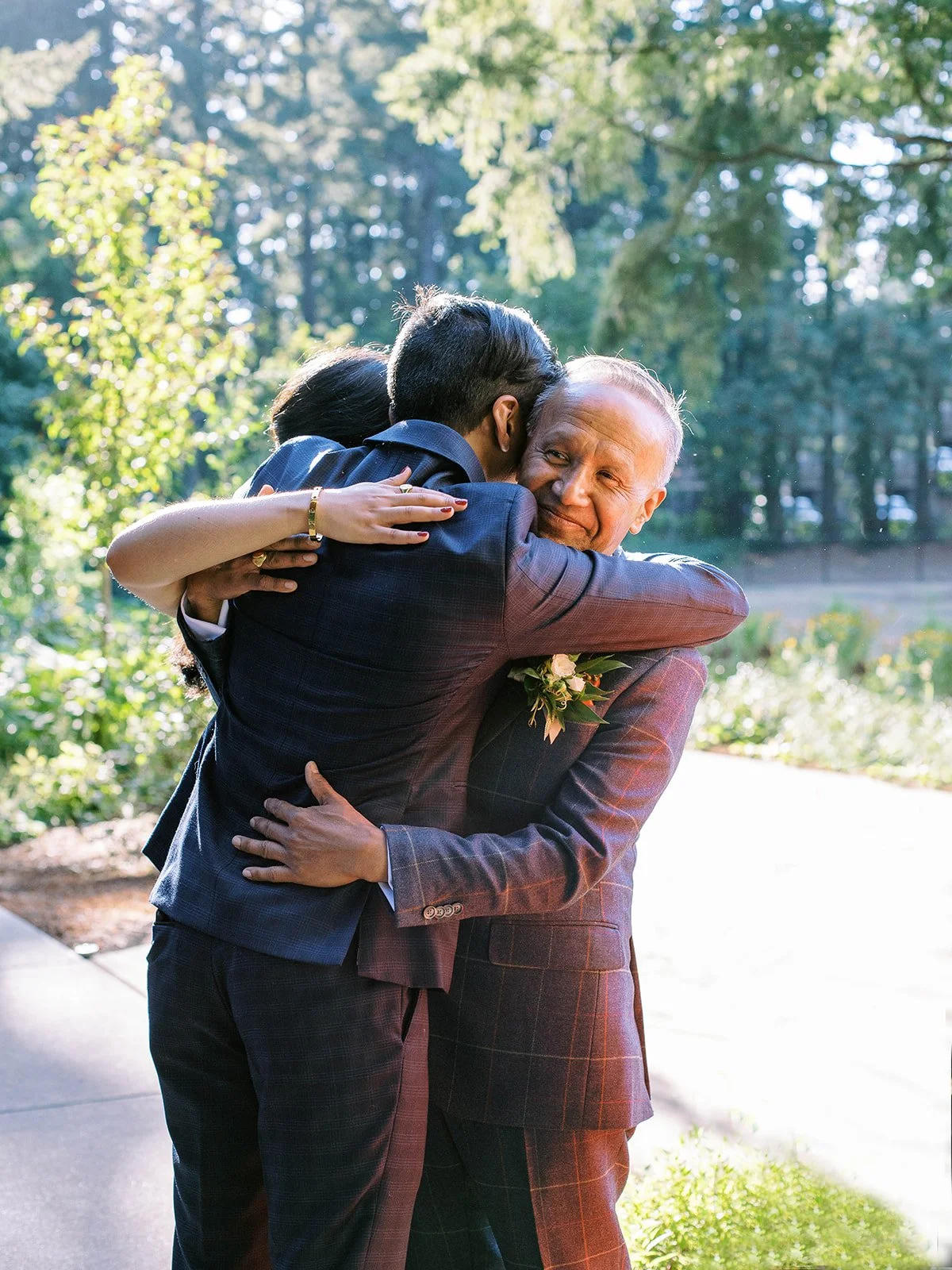 Groom embraces an older wedding guest in the sunlit garden after the ceremony.