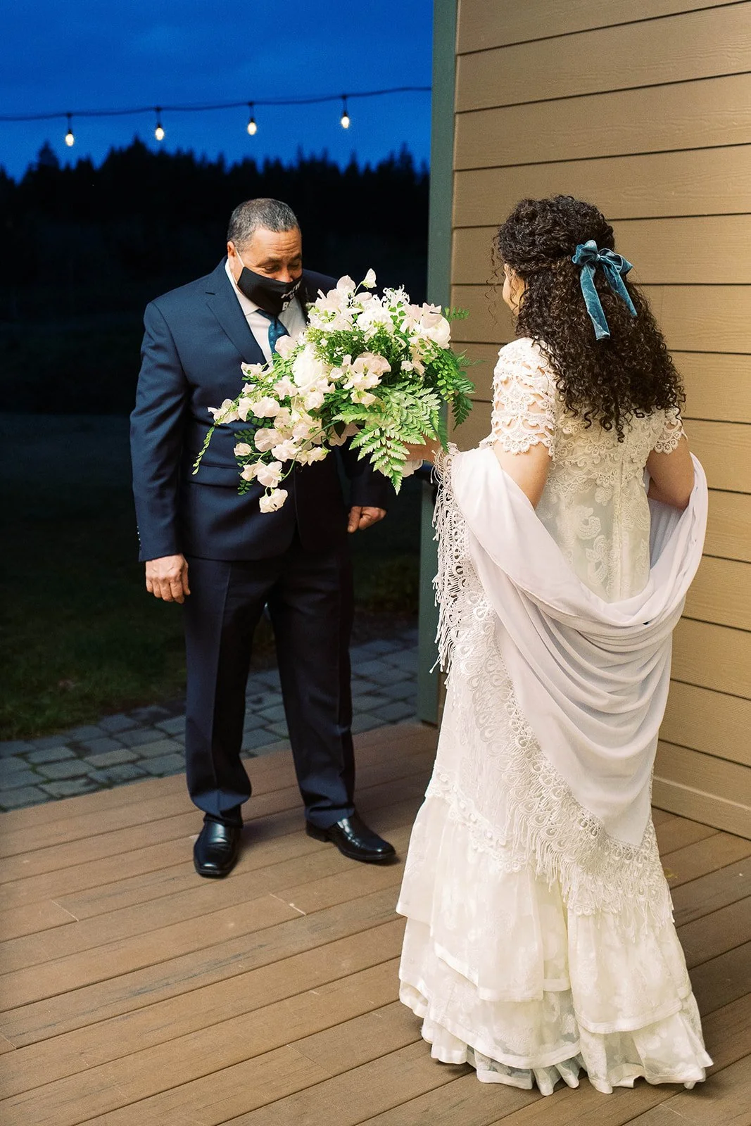 Bride faces her father while holding a cascading bouquet during their first look before the ceremony.