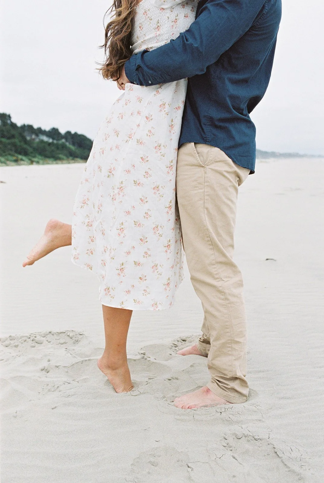 Close-up of couple embracing on beach, woman lifted slightly with bare feet in sand