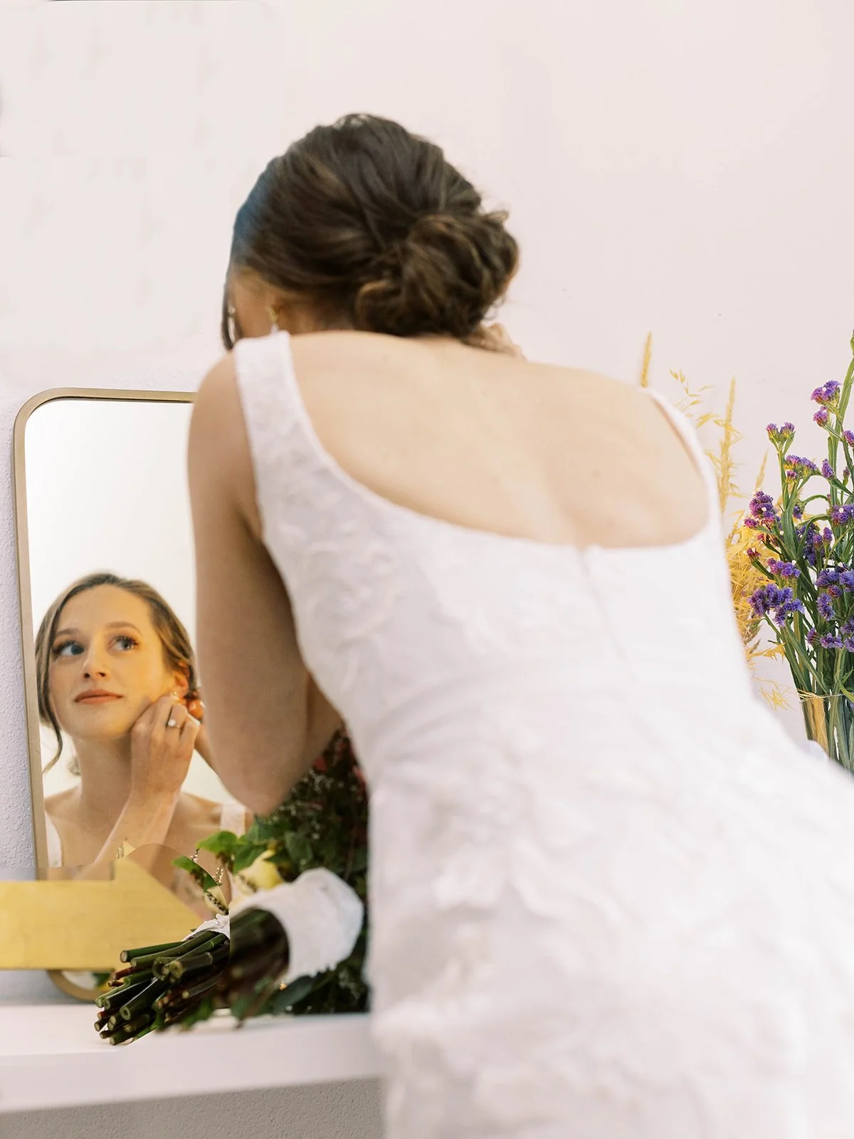 Bride getting ready at a mirror with her bouquet resting nearby.