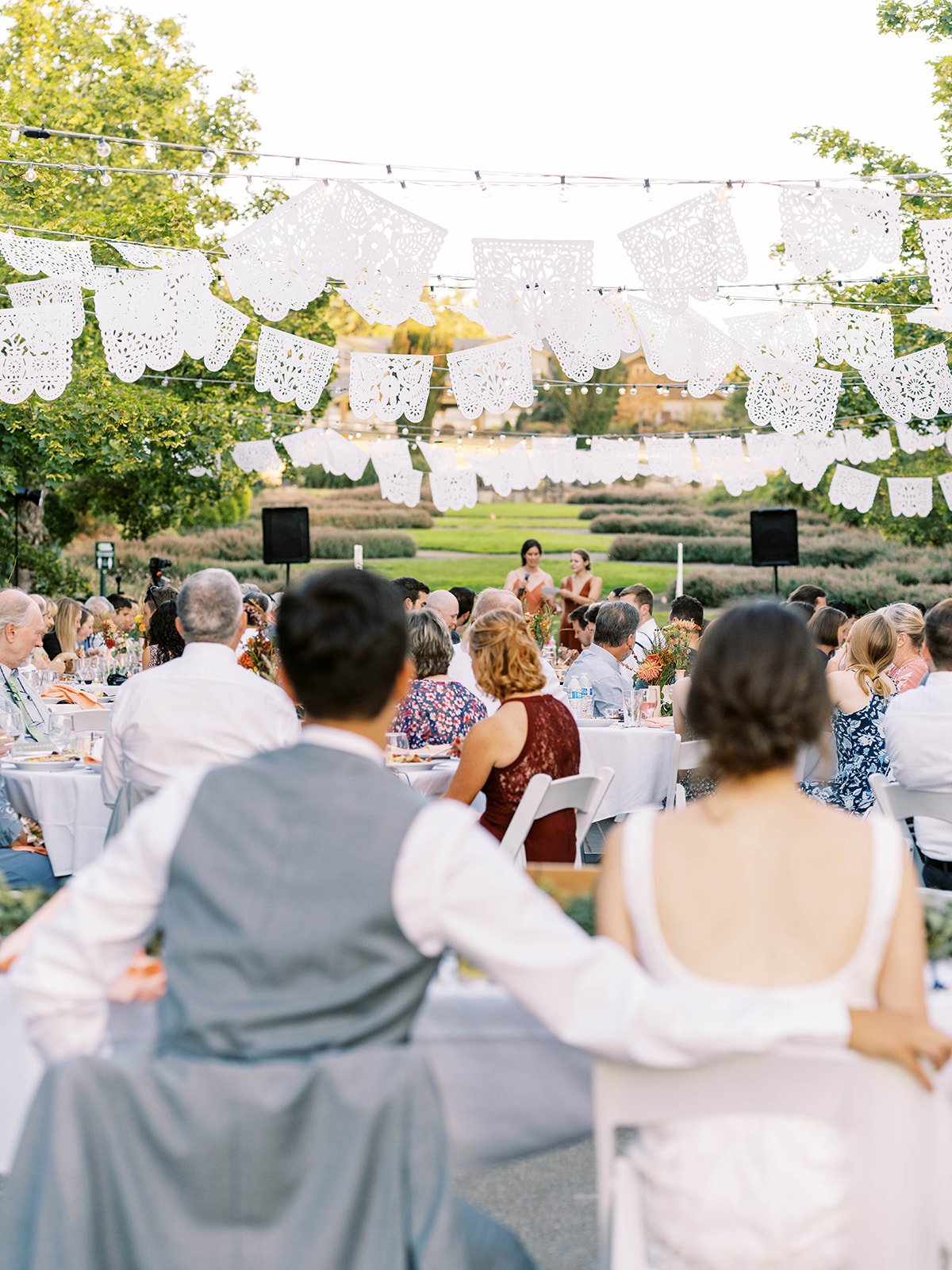 Wedding guests seated beneath white papel picado banners and string lights during an outdoor reception.