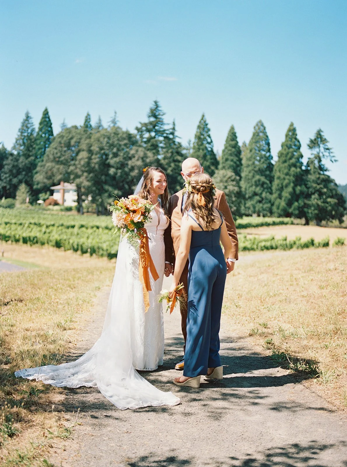 Bride and groom greeting bridesmaid on path during outdoor wedding portraits