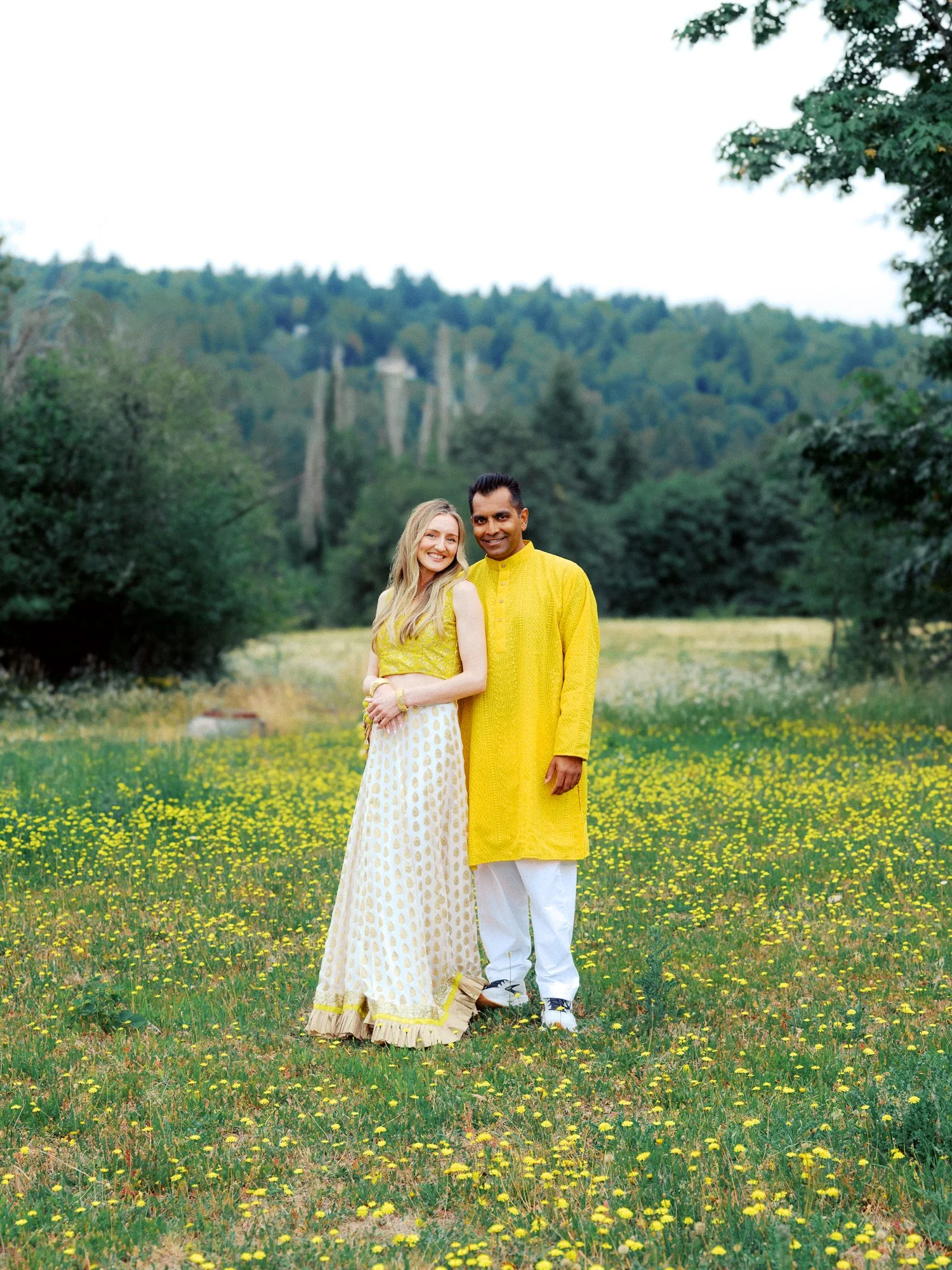 Alacia and Rohit posing together in yellow Haldi attire in a field of wildflowers.
