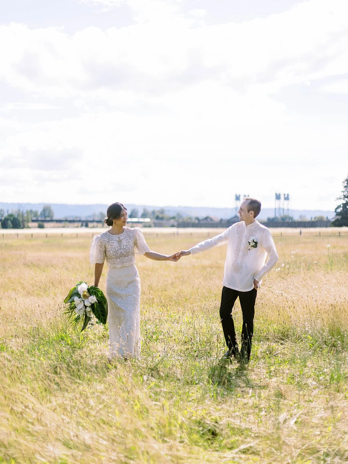 Bride and groom holding hands and smiling at each other while walking through a golden grass field at Pearson Airfield
