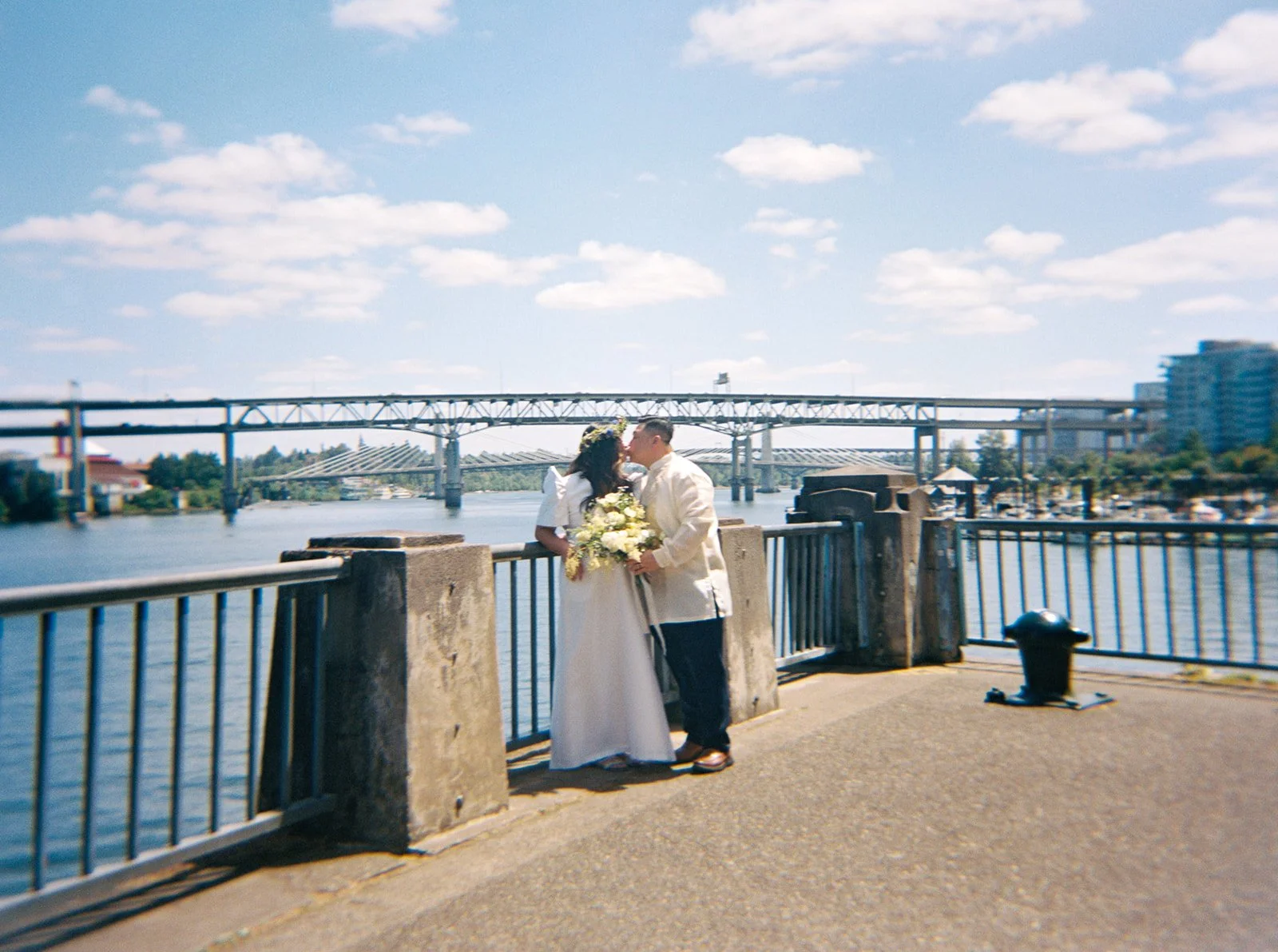 Couple kisses beside the Willamette River during their Portland elopement, with bridges stretching across the background.