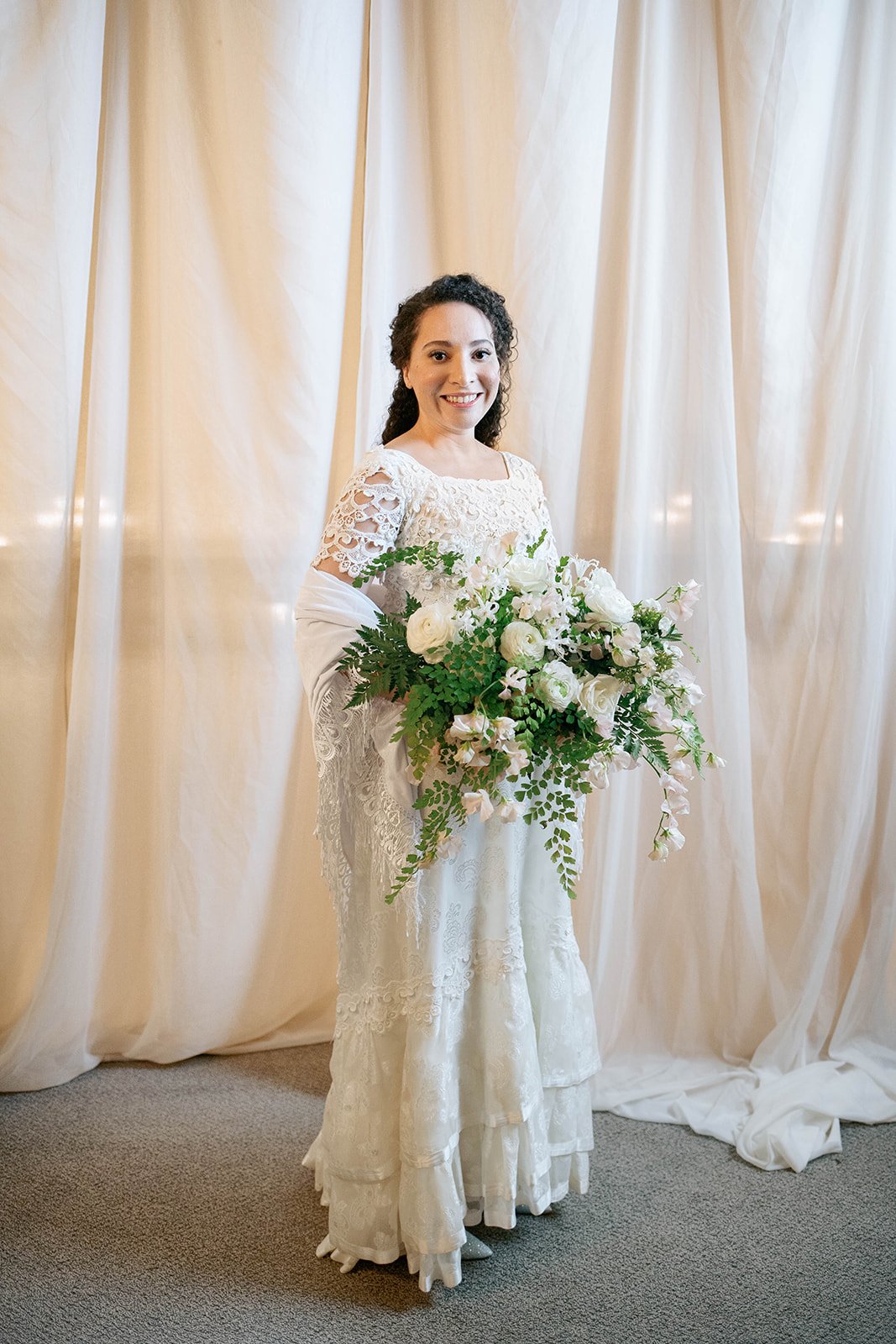 Bride in a vintage lace gown holding a cascading white and green bouquet at her Portland wedding.