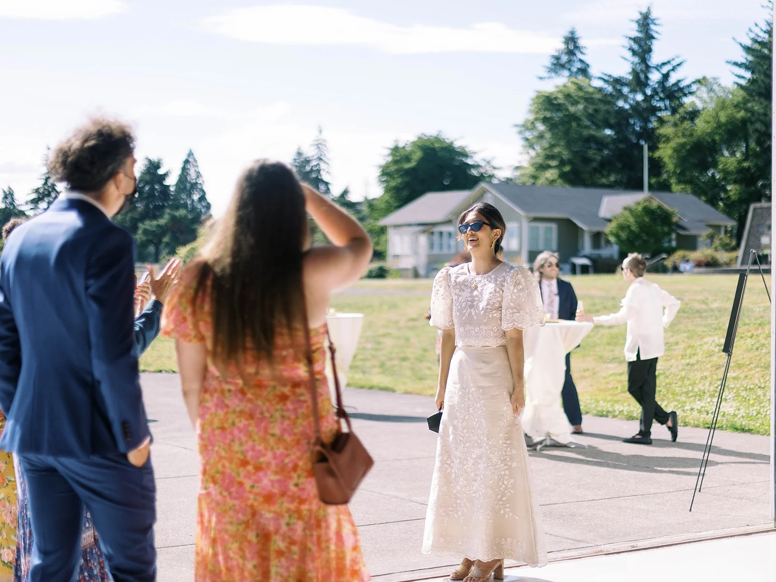 Bride in sunglasses and embroidered Filipino gown laughing while greeting wedding guests on the airfield tarmac
