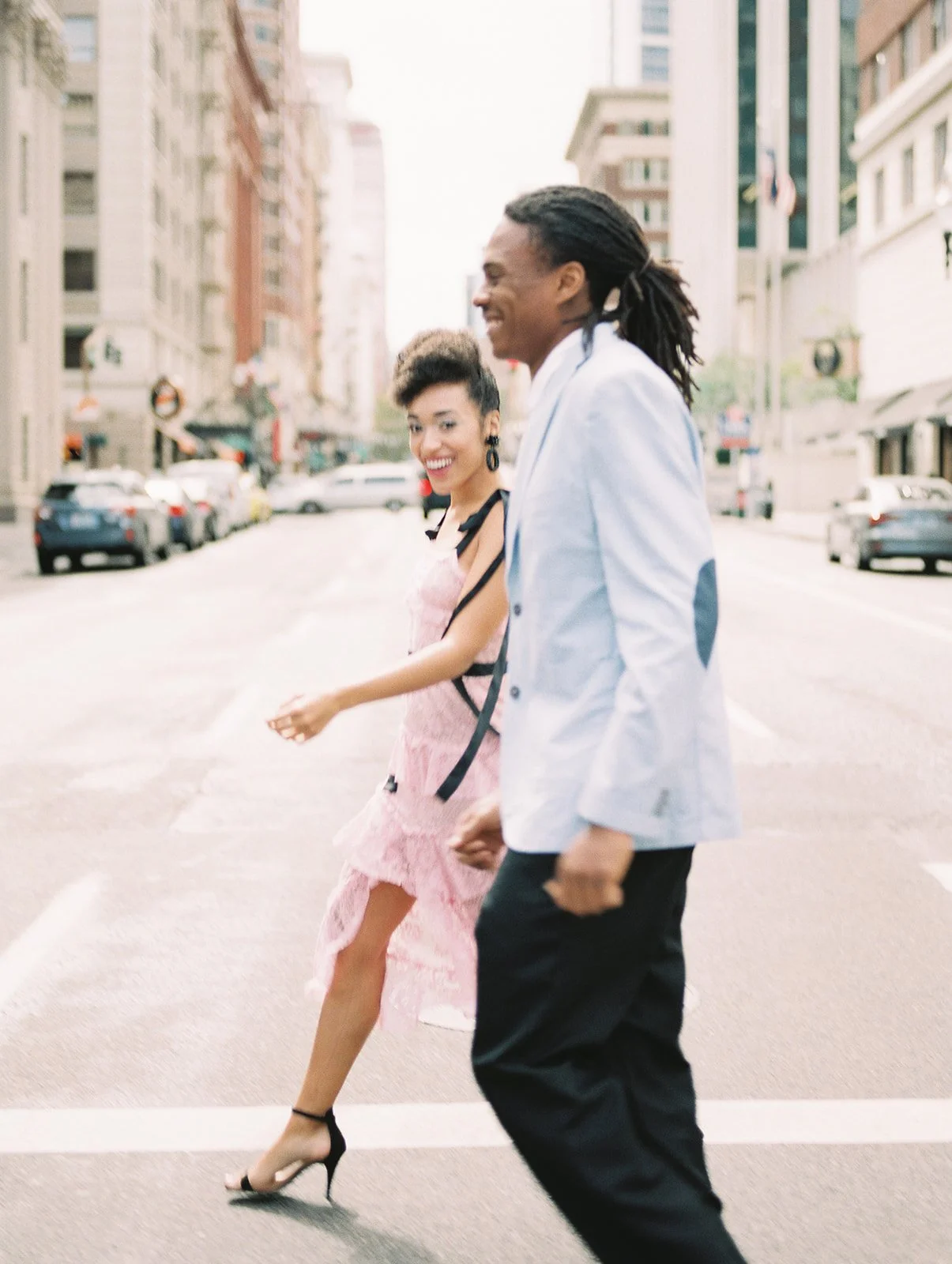 Couple walking across downtown Portland street, woman in pink dress and man in light blue blazer