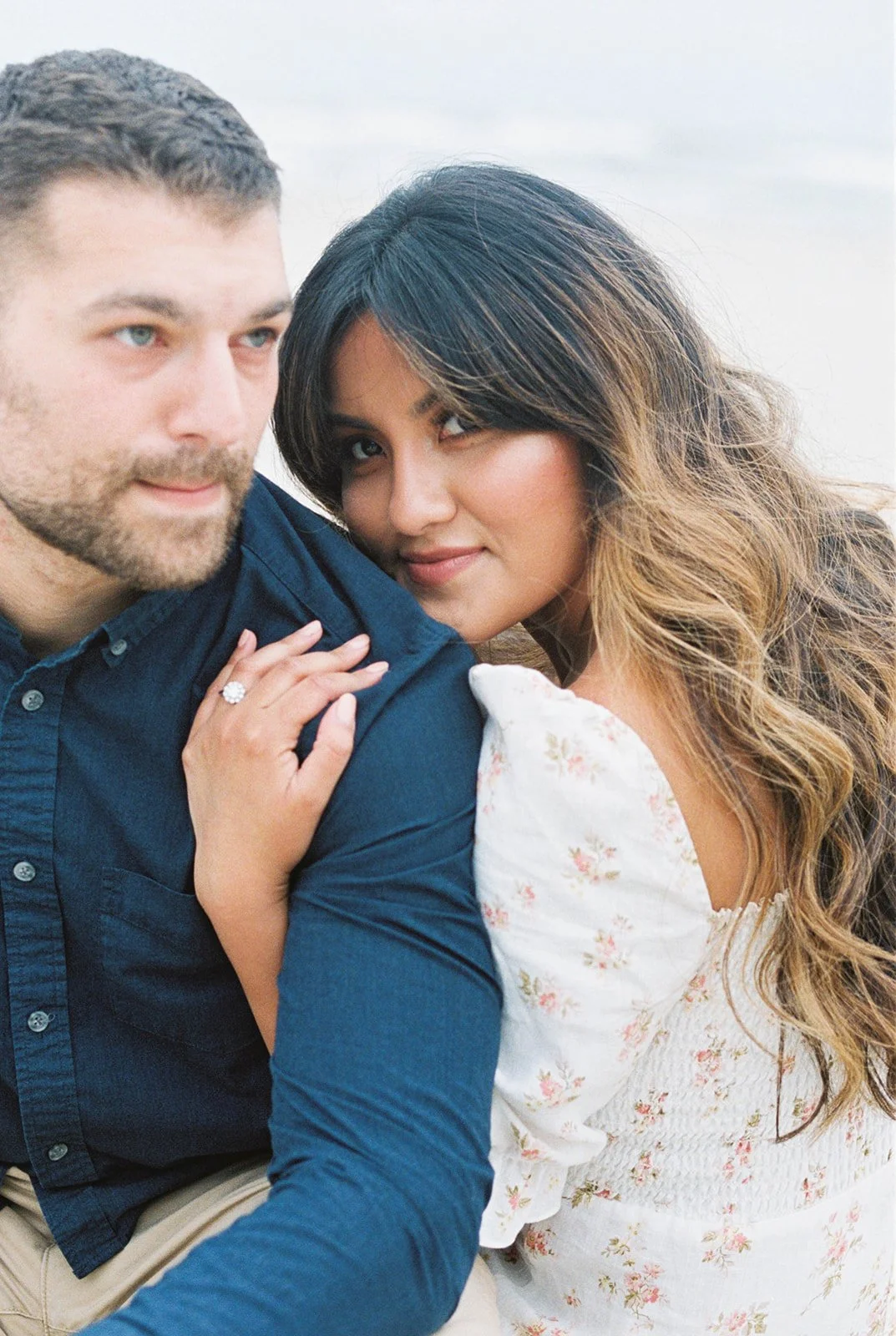 Intimate portrait of couple, woman leaning on man’s shoulder showing engagement ring