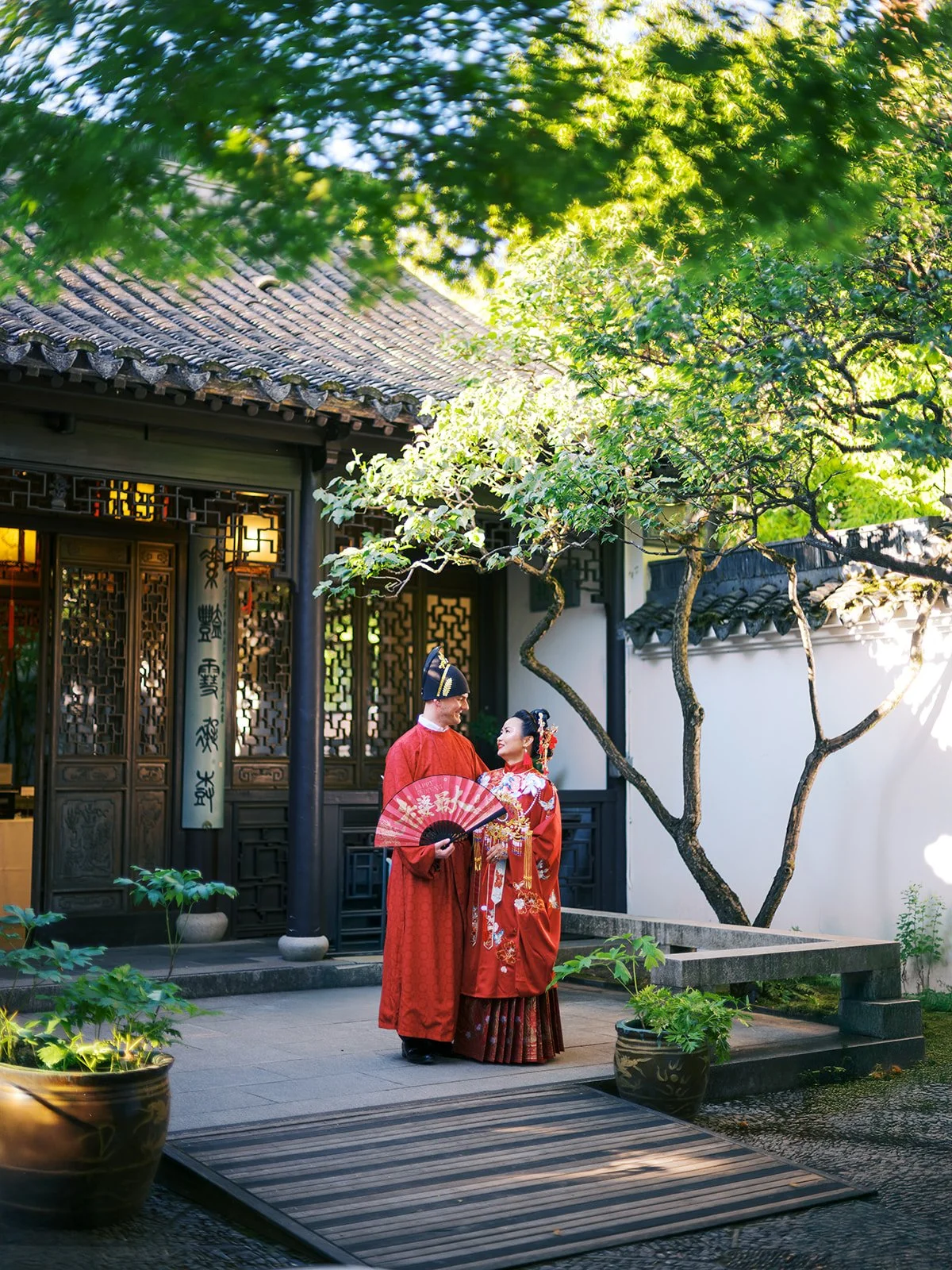 Couple wearing traditional red Chinese wedding attire in a classical Chinese garden