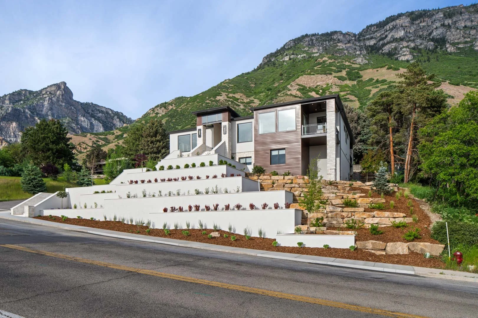 Terraced front yard landscape design with foam block and natural rock retaining walls, layered plantings, and panoramic mountain views.