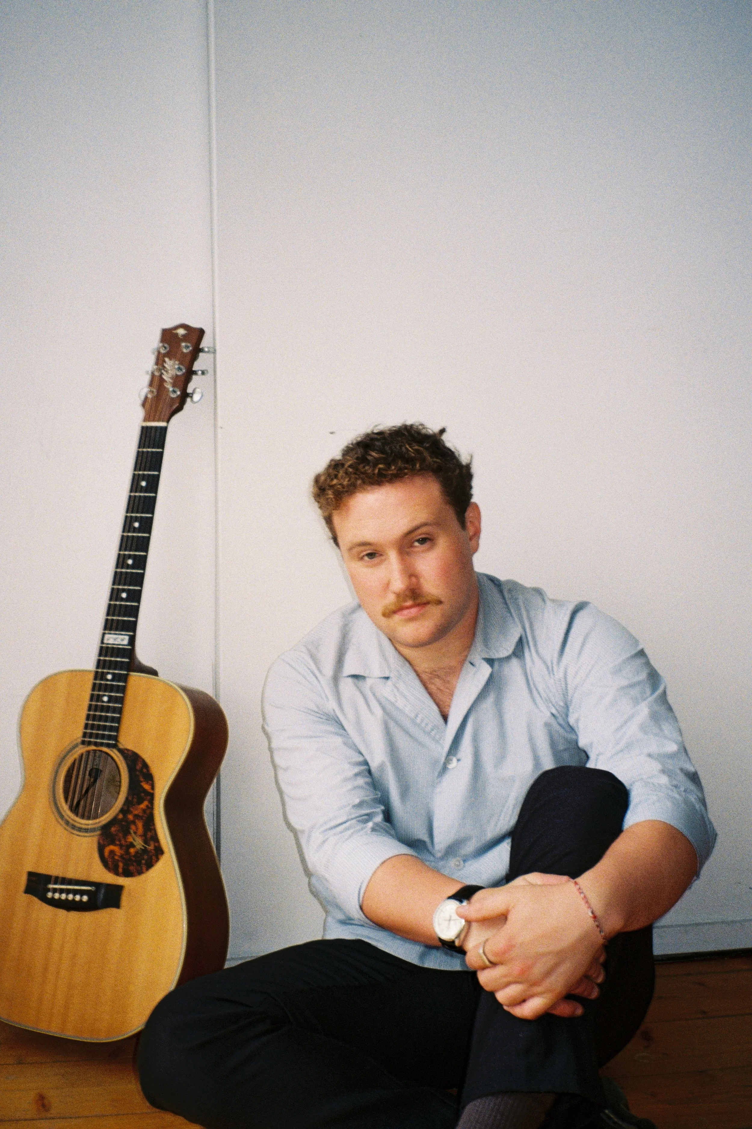 James, sitting on the floor with an acoustic guitar beside him