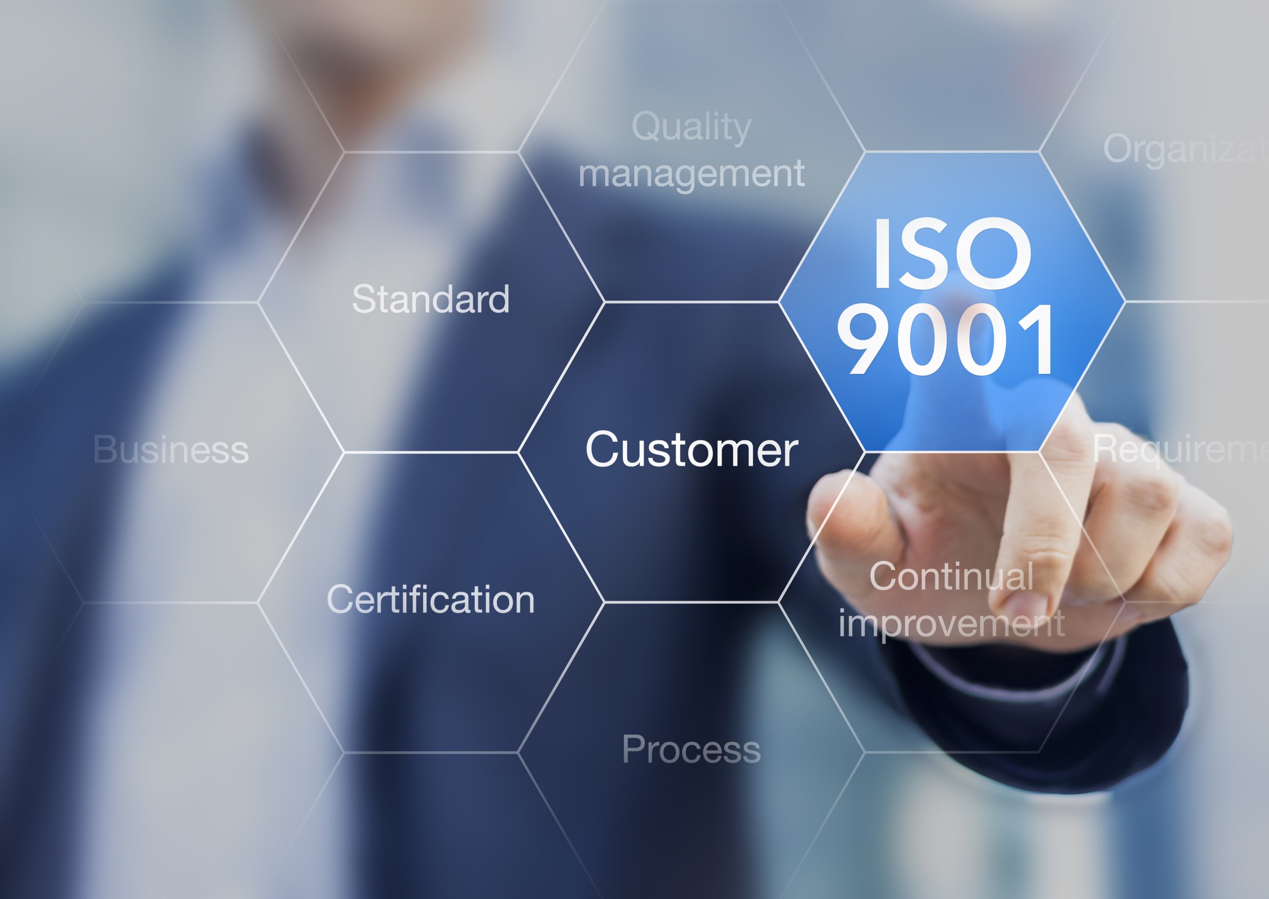 A person in a business suit points at a digital hexagon diagram with words related to quality management, standards, customer focus, and process improvement, emphasizing ISO 9001 certification.