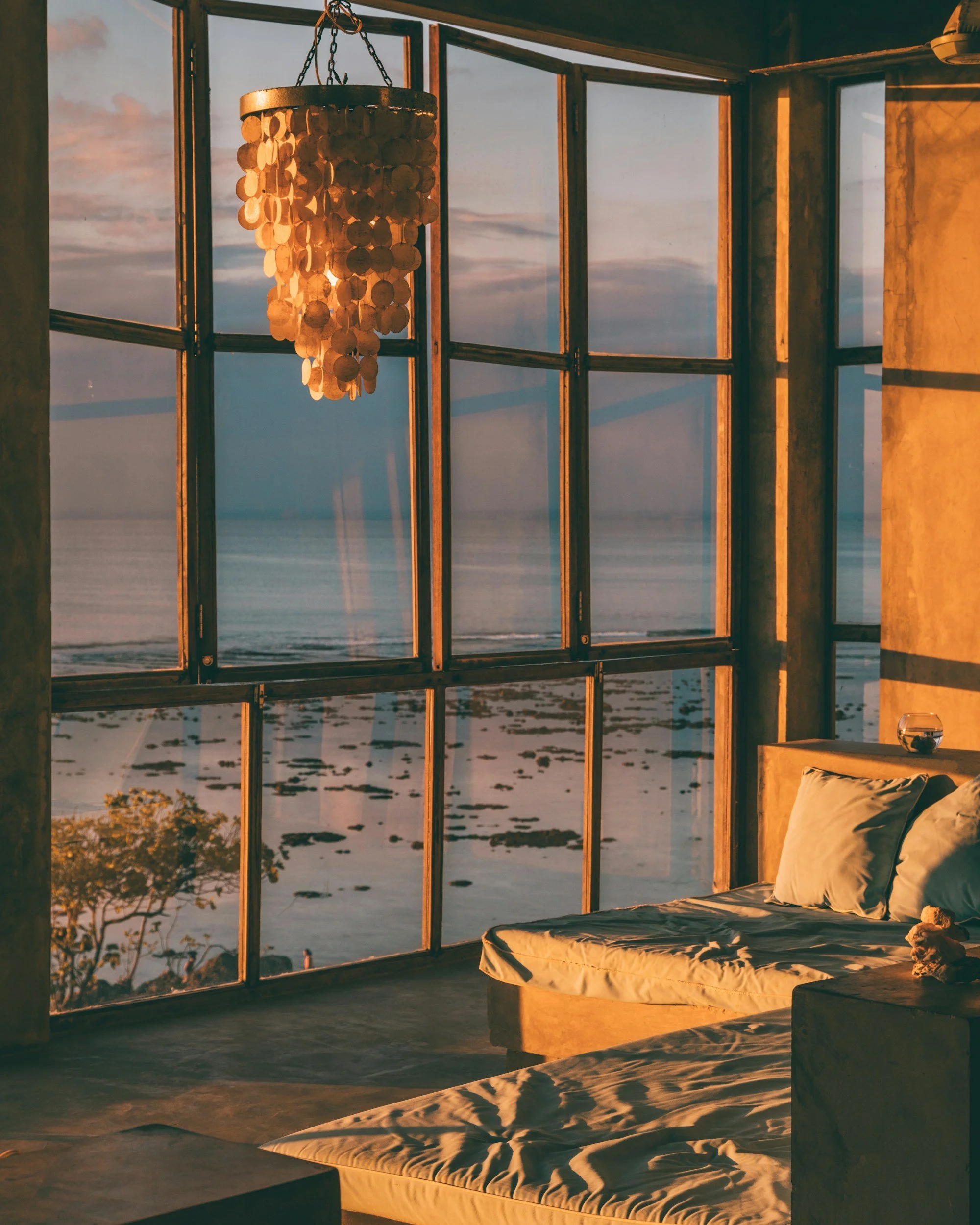 A luxury home living room decorated with stone walls and a beautiful chandelier overlooking an ocean view window