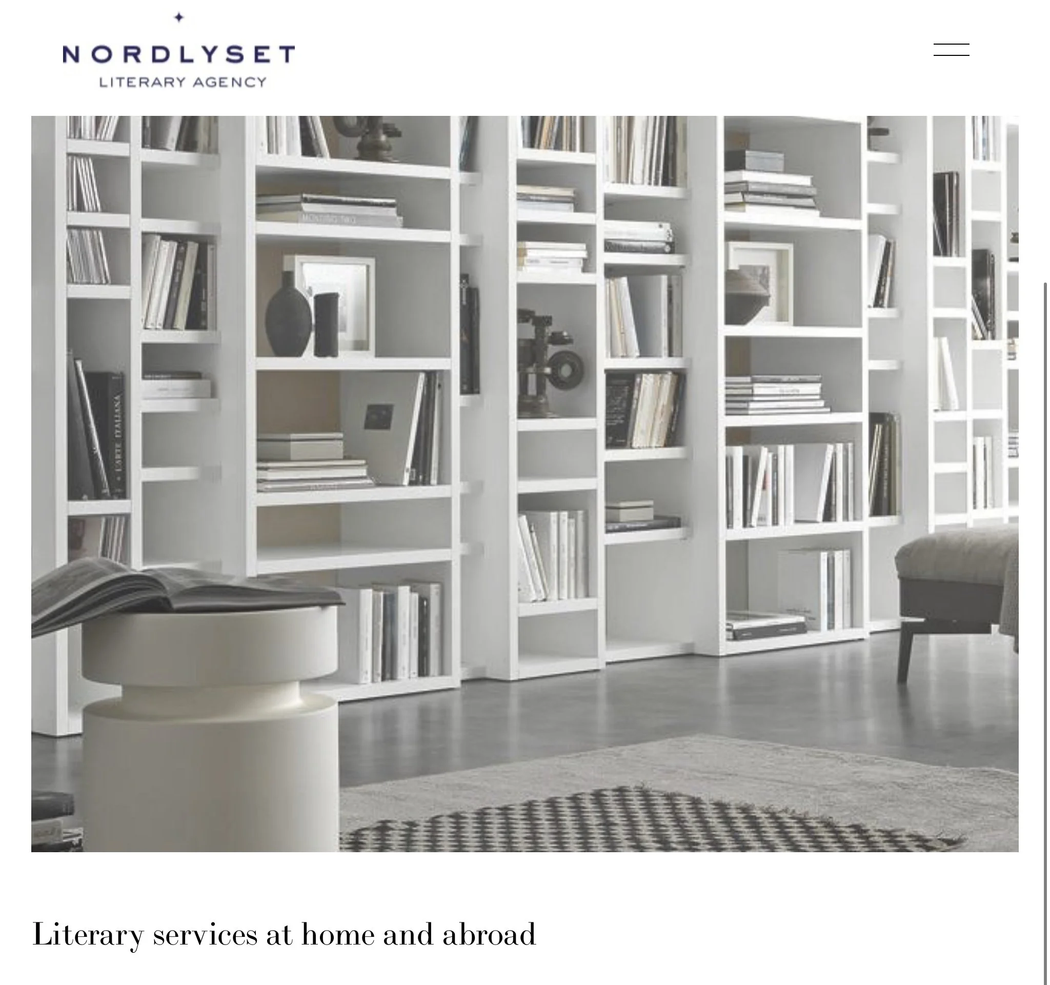 A modern white bookshelf filled with books and decorative objects in a living room with a gray sofa, a round side table with an open book, and a patterned rug.