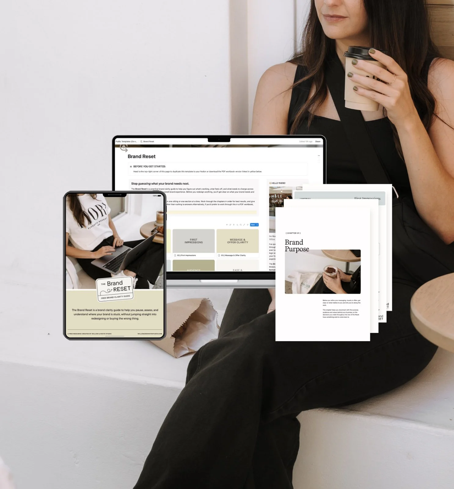 A woman sitting on a white bench holding a cup of coffee, with a laptop, smartphone, and printed documents displaying a brand reset guide in front of her.