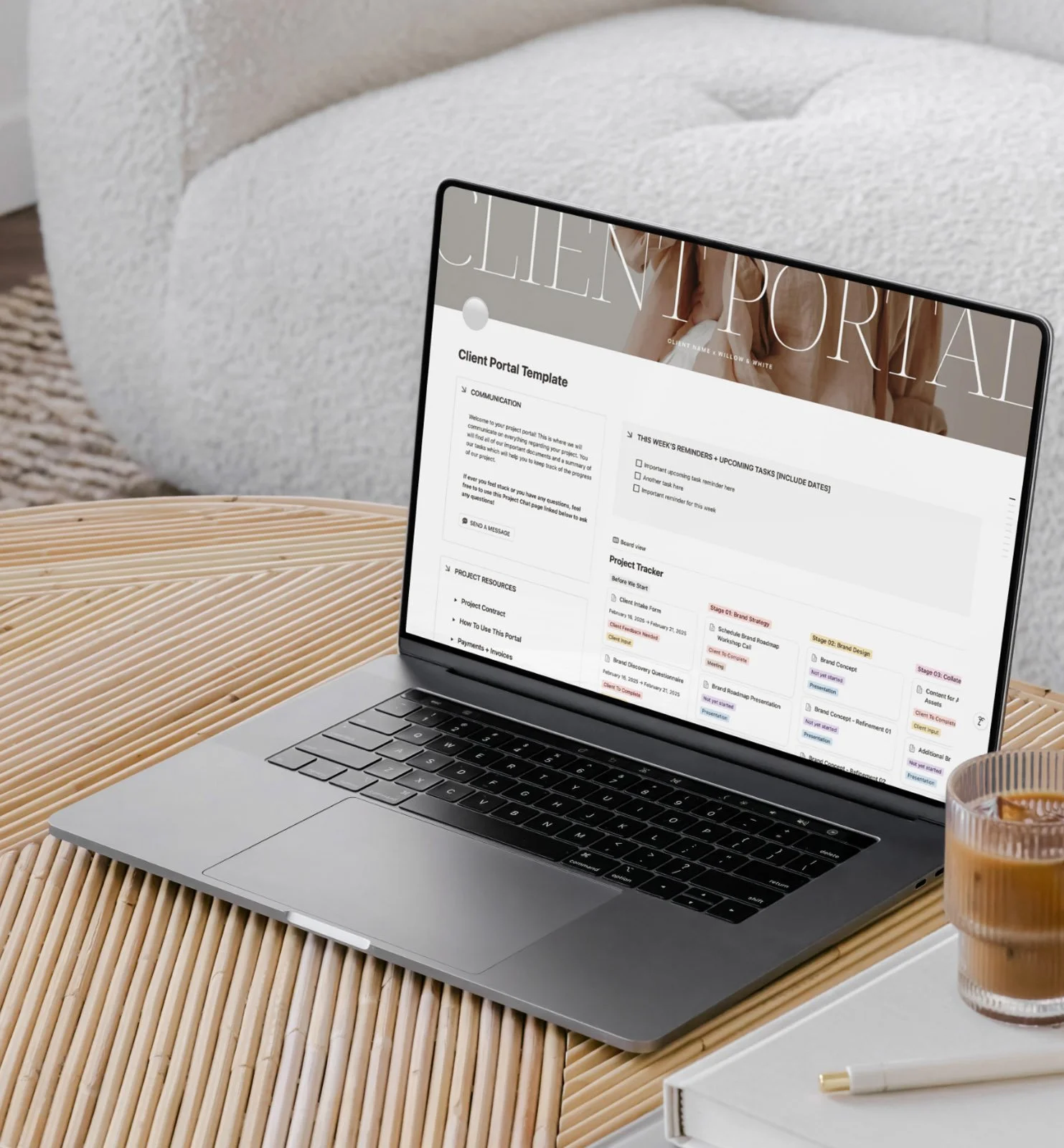A laptop displaying a project management portal on a wooden table, with a glass of iced coffee and a pen nearby.