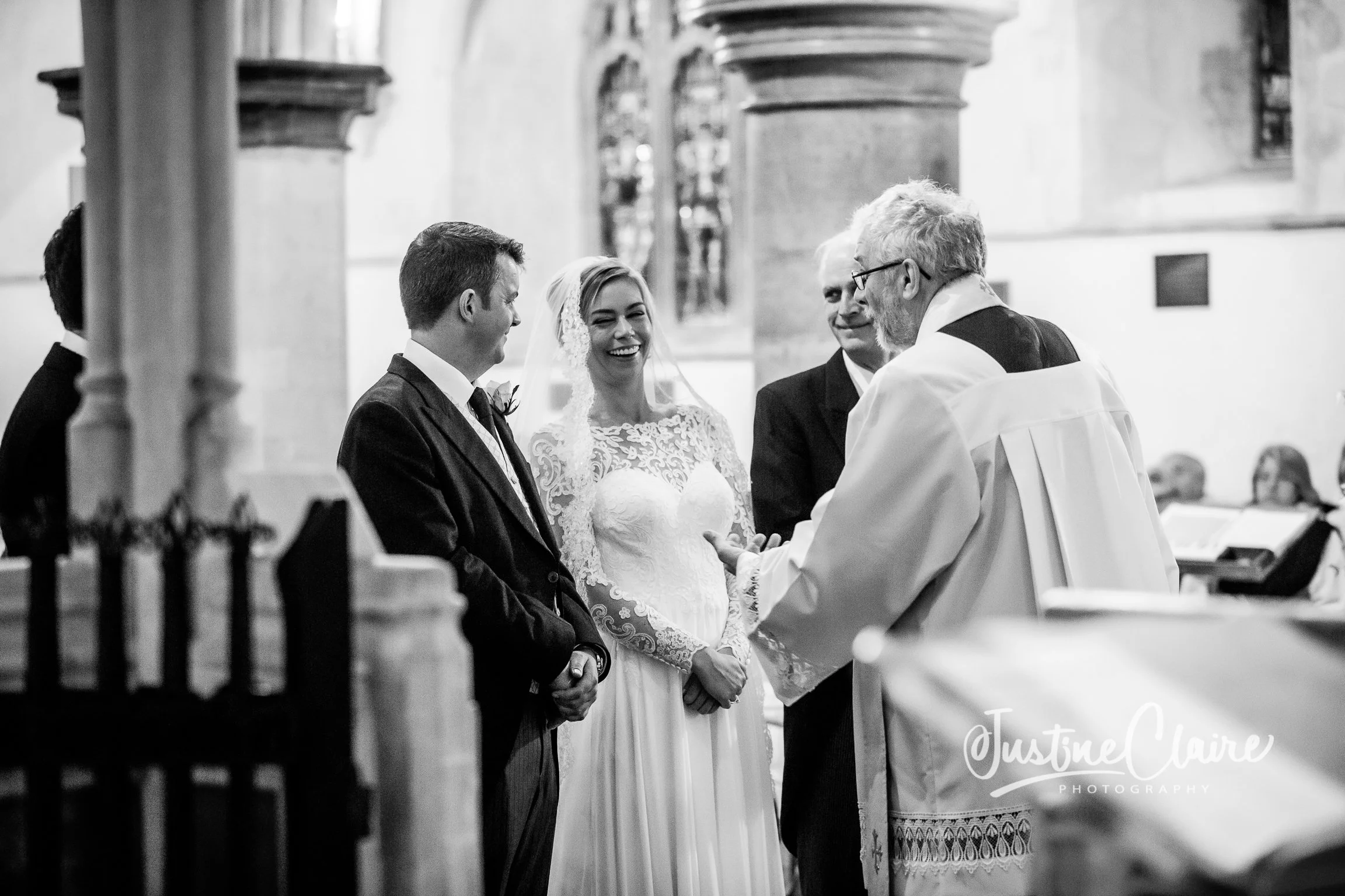 Bride and groom standing before a priest during a wedding ceremony in a church, with guests watching in the background.