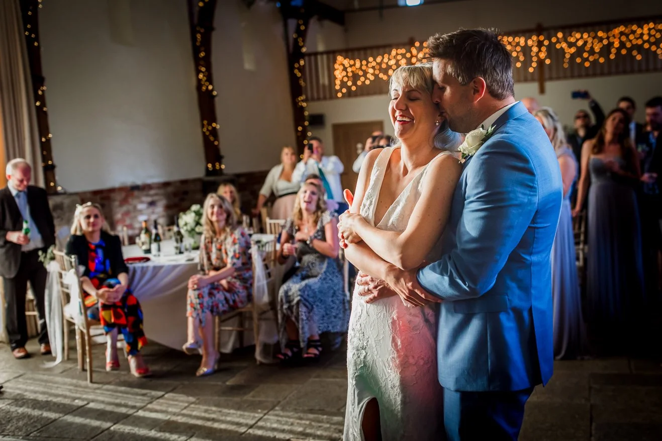 A bride and groom dancing at their wedding reception, with guests watching and smiling in the background.