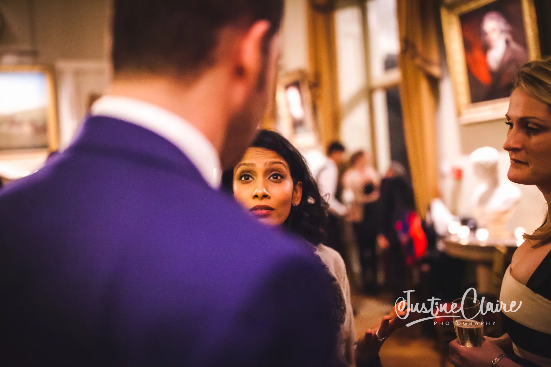 Three people in conversation at an indoor art gallery or museum, with paintings and sculptures in the background. Goodwood House