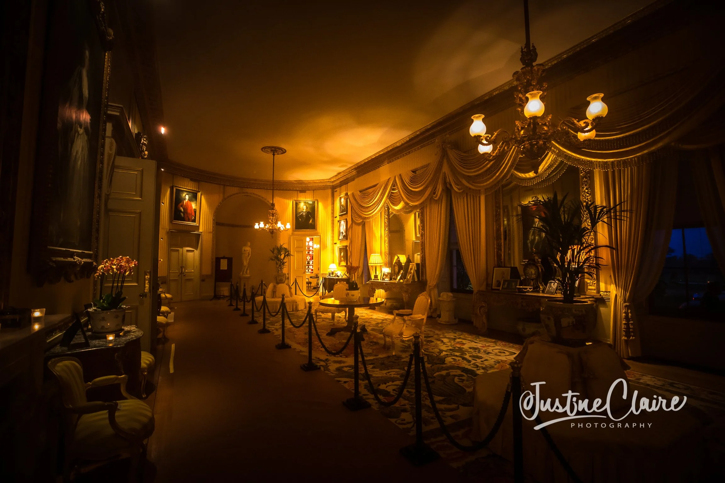 An elegant, richly decorated living room with warm lighting, ornate drapes, classical paintings, and vintage furniture.