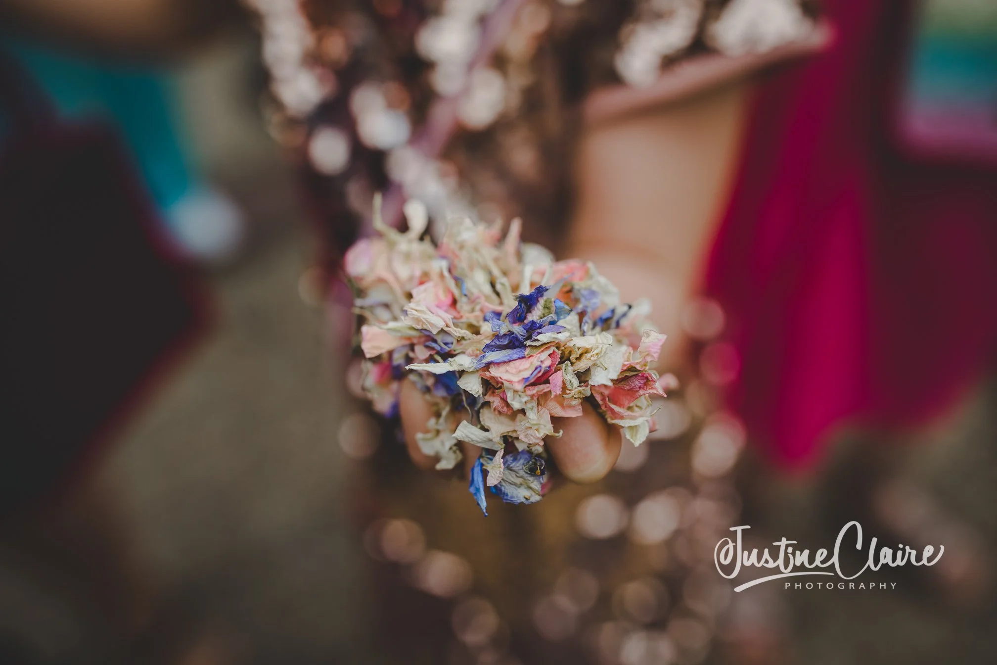 A person holding a bouquet of dried, multicolored flowers, with a blurred colorful background and the text 'JustineClaire Photography' at the bottom right corner.