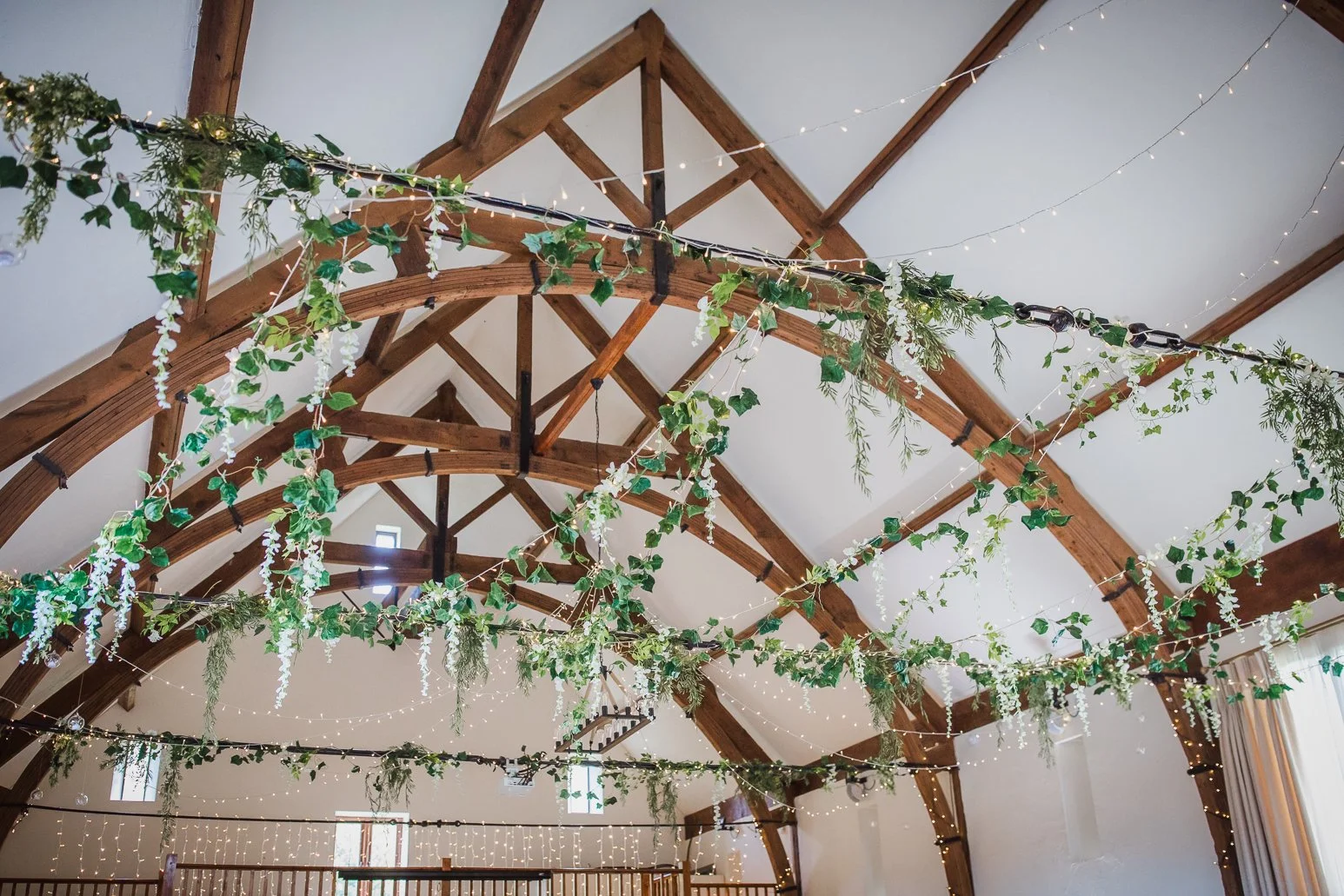 Decorative ceiling with green garland, ivy, hanging lights, and wooden beams in a rustic venue.