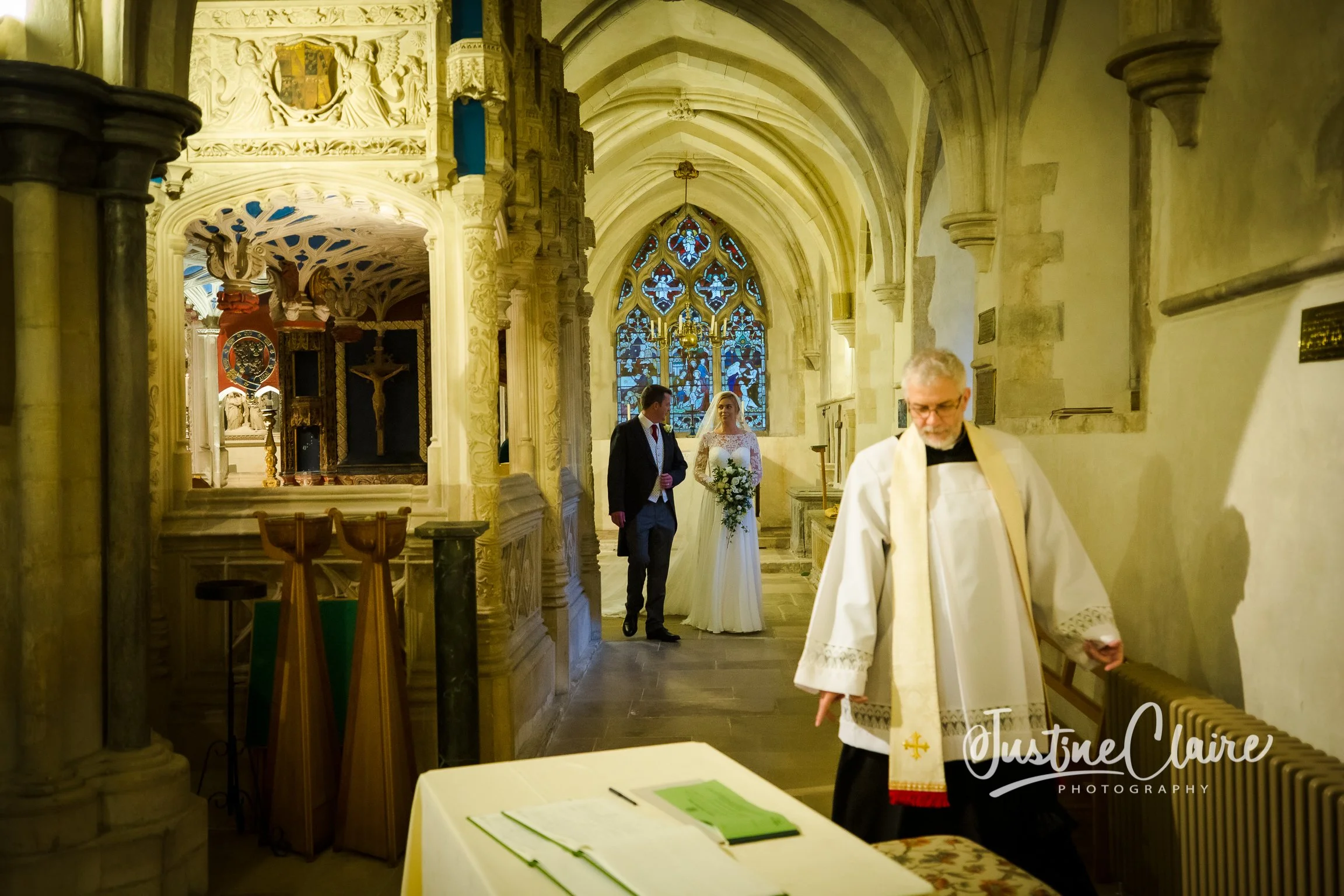 A bride and groom walking down the aisle in a church, with a priest standing nearby.