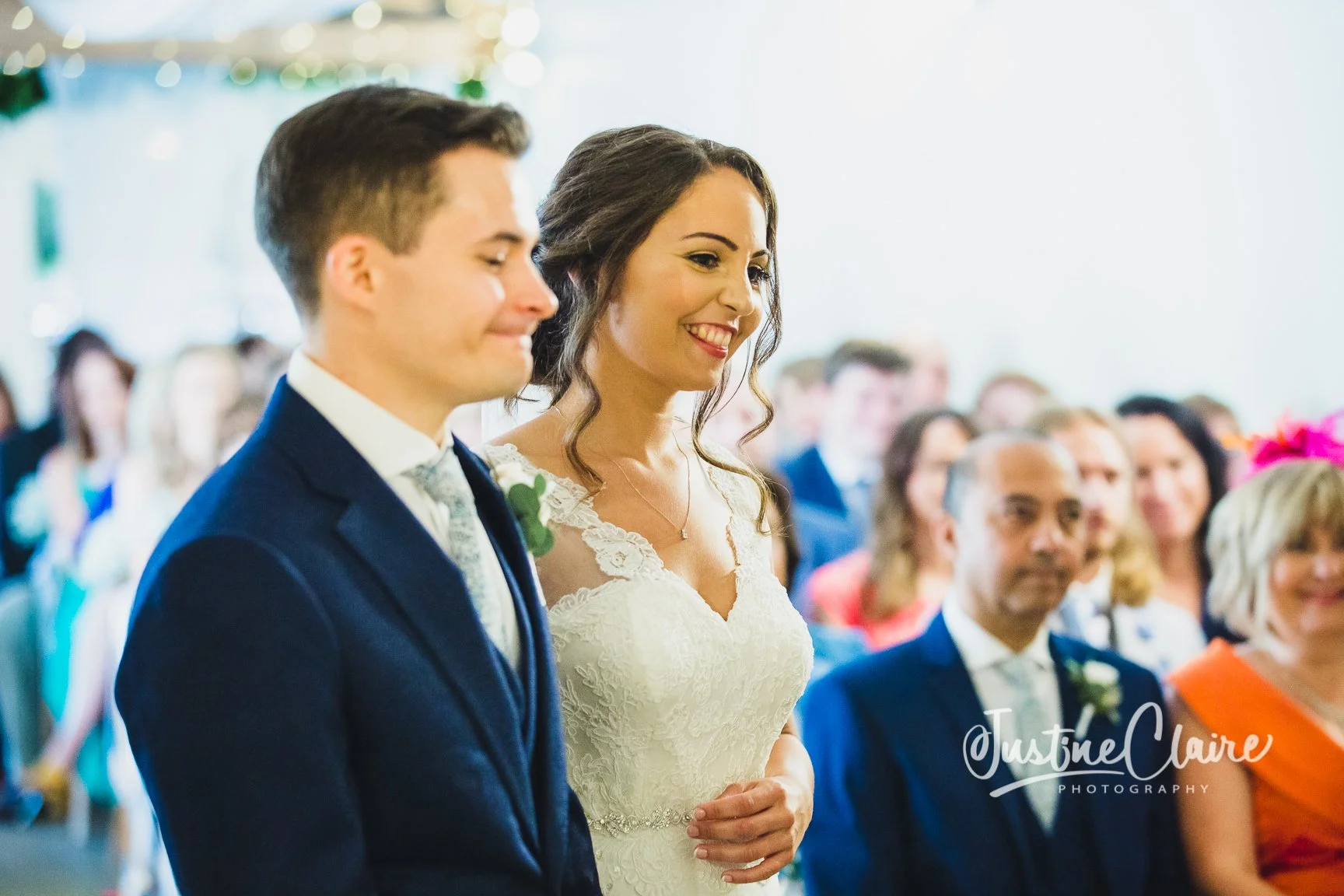A bride and groom standing side by side during a wedding ceremony, smiling as they listen.