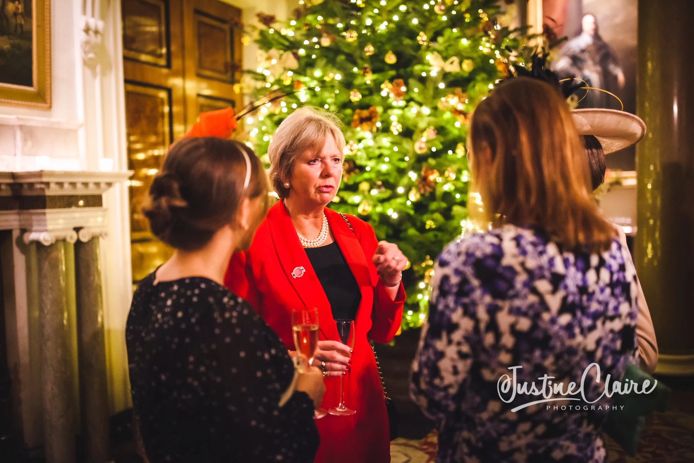 Women having a conversation at a holiday party in front of a decorated Christmas tree.