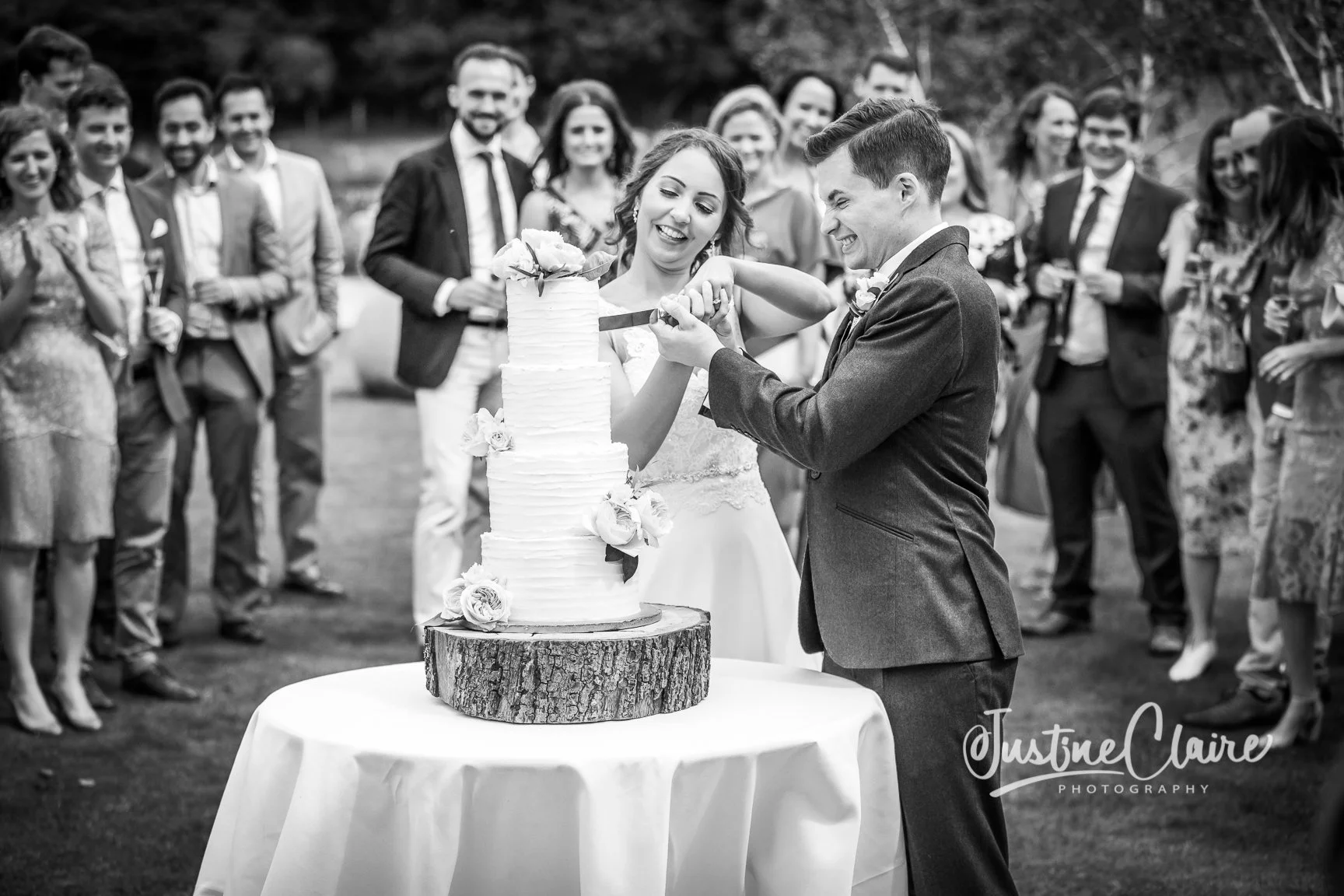 A bride and groom cut a wedding cake outdoors with guests watching and smiling. Farbridge gorgeous wedding venue chichester