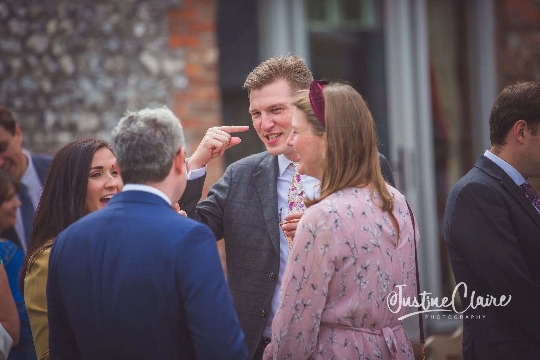 Group of people socializing at an outdoor event, smiling and engaging in conversation, with a woman holding a wine glass and others dressed in suits and dresses.