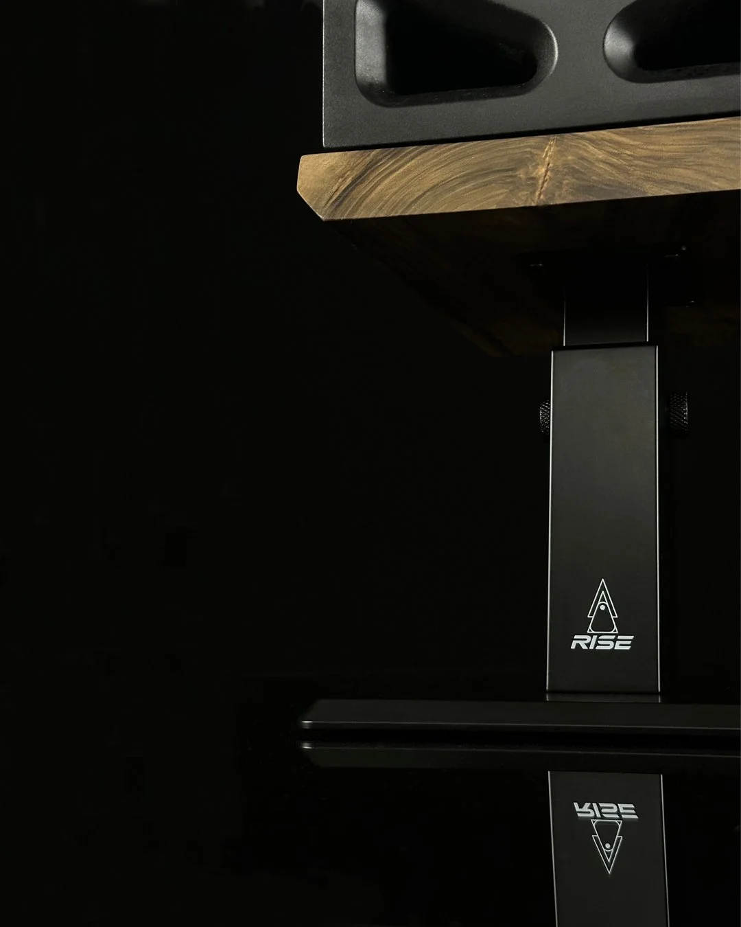 Rise Audio adjustable studio monitor stand with a solid walnut platform on a black background