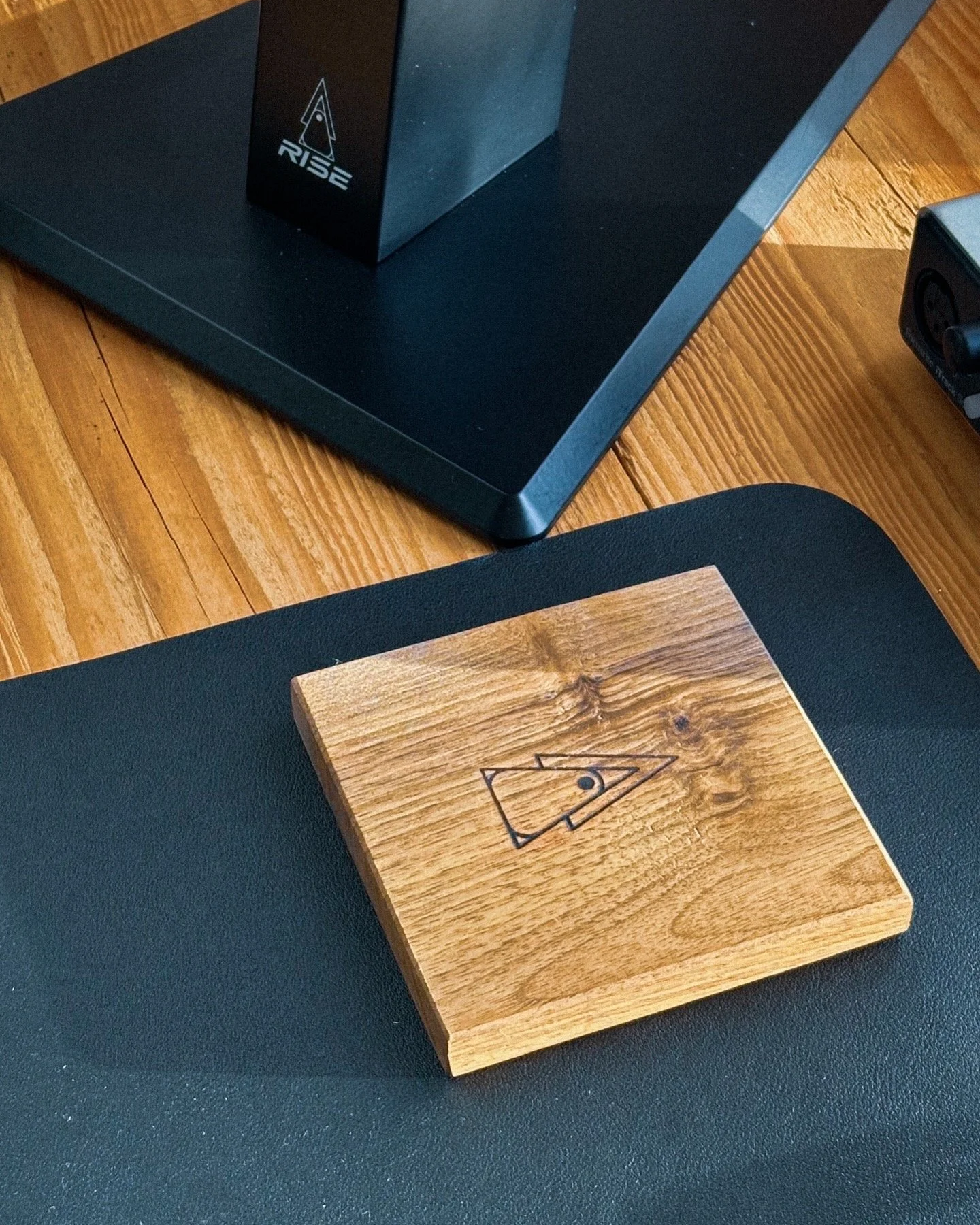 Rise Audio walnut coaster on a desk beside a studio monitor stand