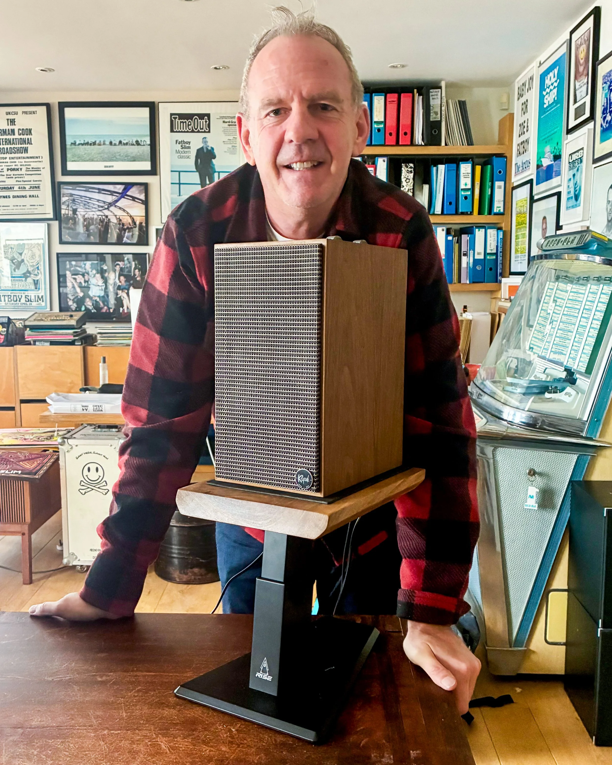 Fatboy Slim with a speaker on a Rise Audio walnut studio monitor stand